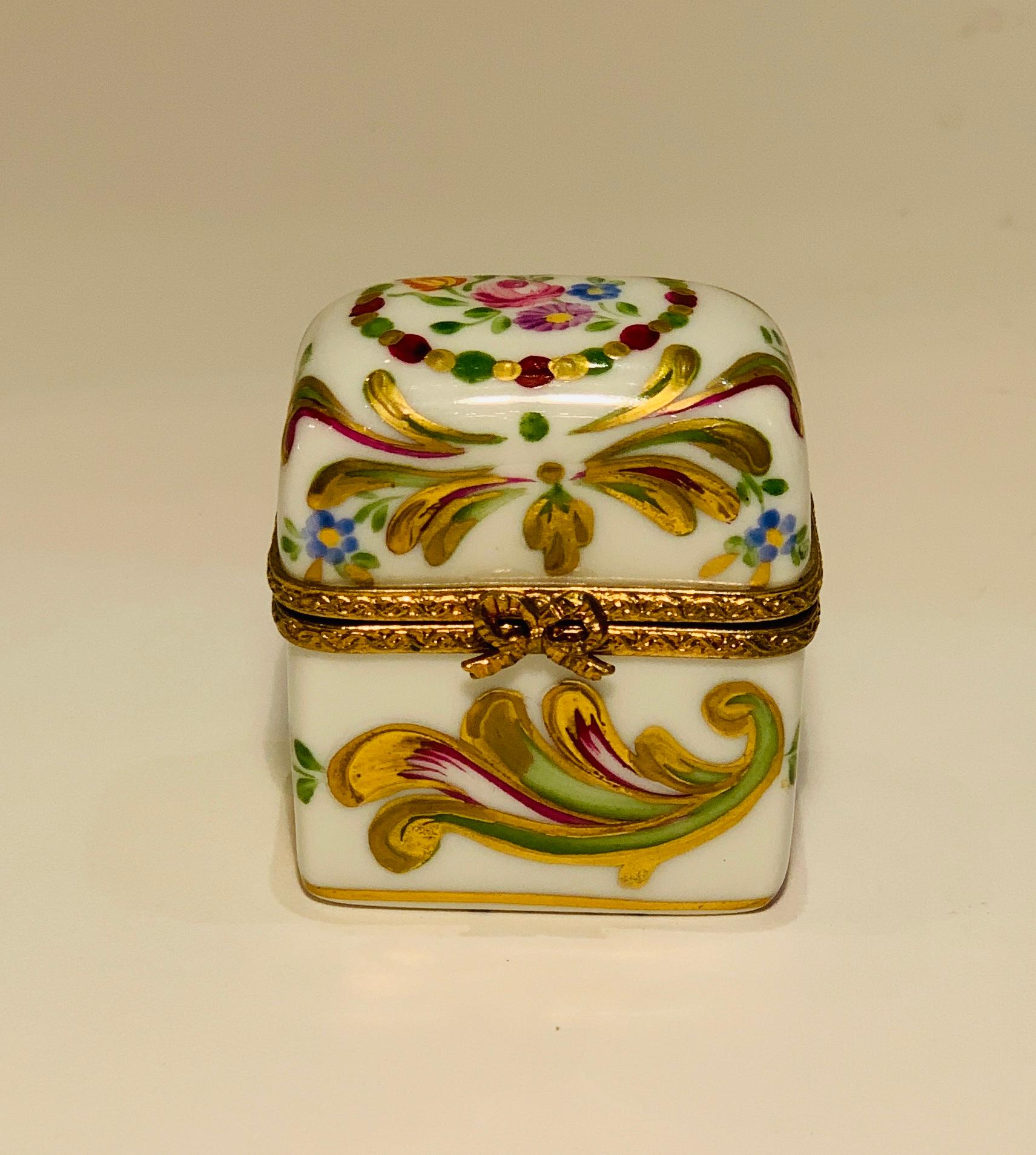 Exquisitely handmade and hand painted vintage miniature Limoges porcelain box with a hinged lid is decorated with flowers and features lavish flourishes of 24-karat gold. The porcelain box and lid feature rims or fittings of richly patterned gilt