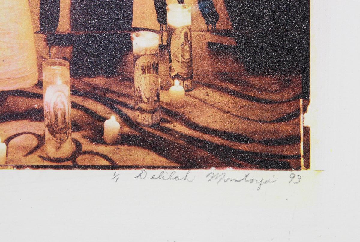 Contemporary photograph on collotype by Houston, TX artist Delilah Montoya. Photograph shows a young woman with long, dark hair with both arms stretched to the sides while surrounded by lit candles. Her back faces the camera as she faces a wall with