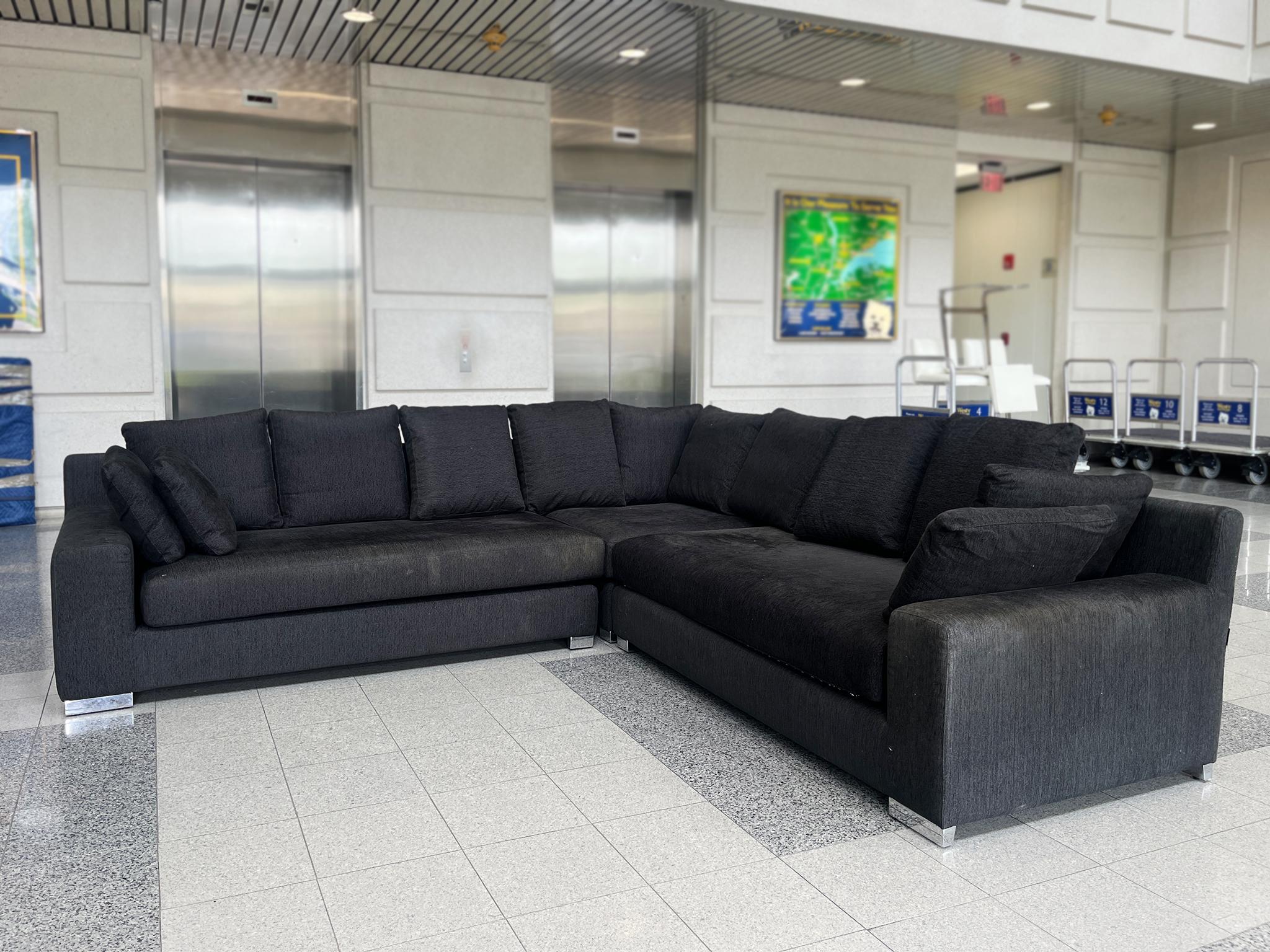 This modern sectional sofa was made by DellaRobbia. It consists of three modular pieces: two long rectangular seats and one square corner seat that come together to form an L-shaped arrangement. The upholstery is a black wool weave while and the