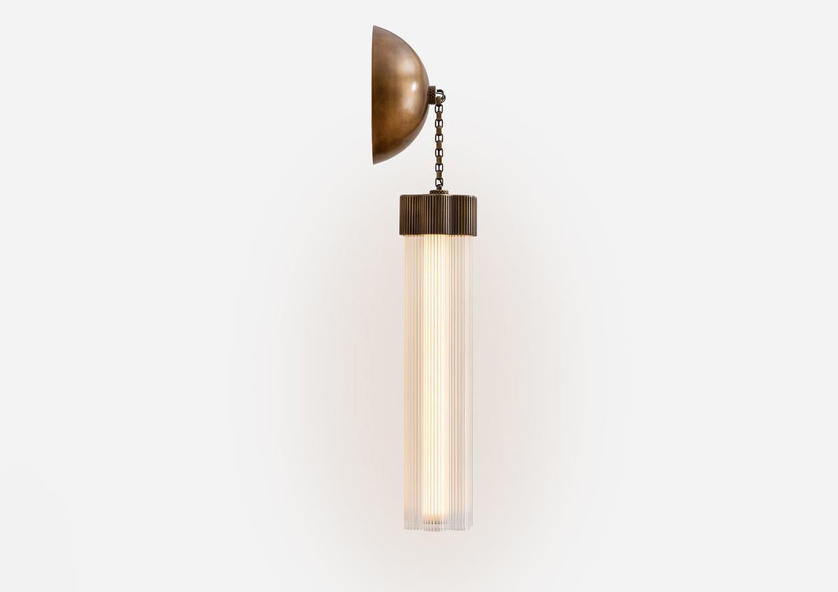 Delphi, eine vielseitige neue Beleuchtungskollektion von Jamie Gray, besteht aus gegossenem und bearbeitetem Messing, gepaart mit geriffelten Glasrohren und ist eine Hommage an ikonische griechische Säulen. Die firmeneigene Messingkette ermöglicht
