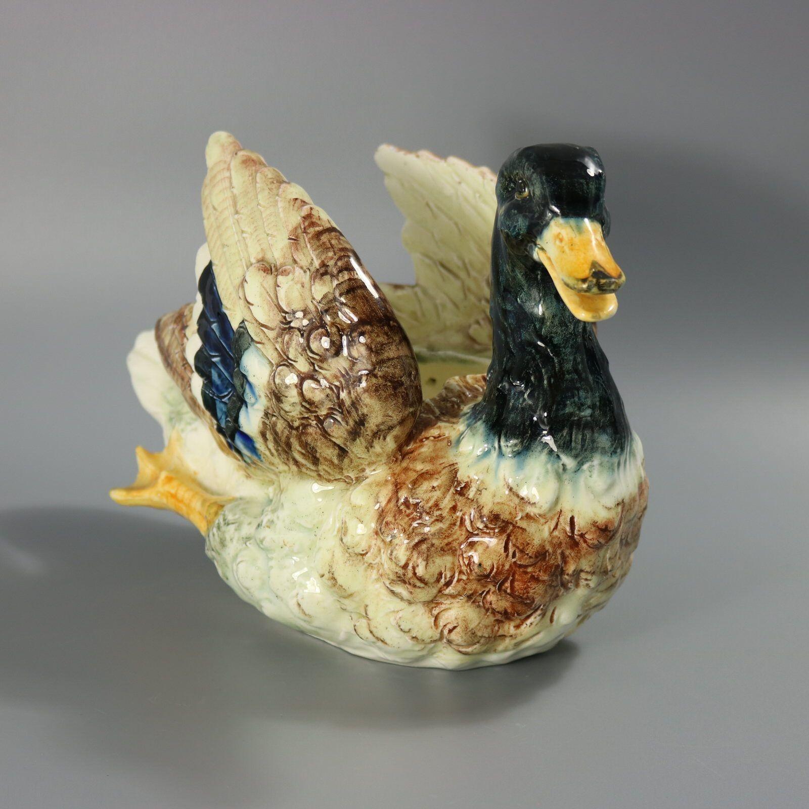 Fioriera in maiolica francese di Delphin Massier che raffigura un'anatra domestica in posizione di nuoto, con le ali arricciate dietro. Colorazione: predominano il crema, il blu acqua e l'ocra. Il pezzo reca il marchio della ceramica Delphin Massier.