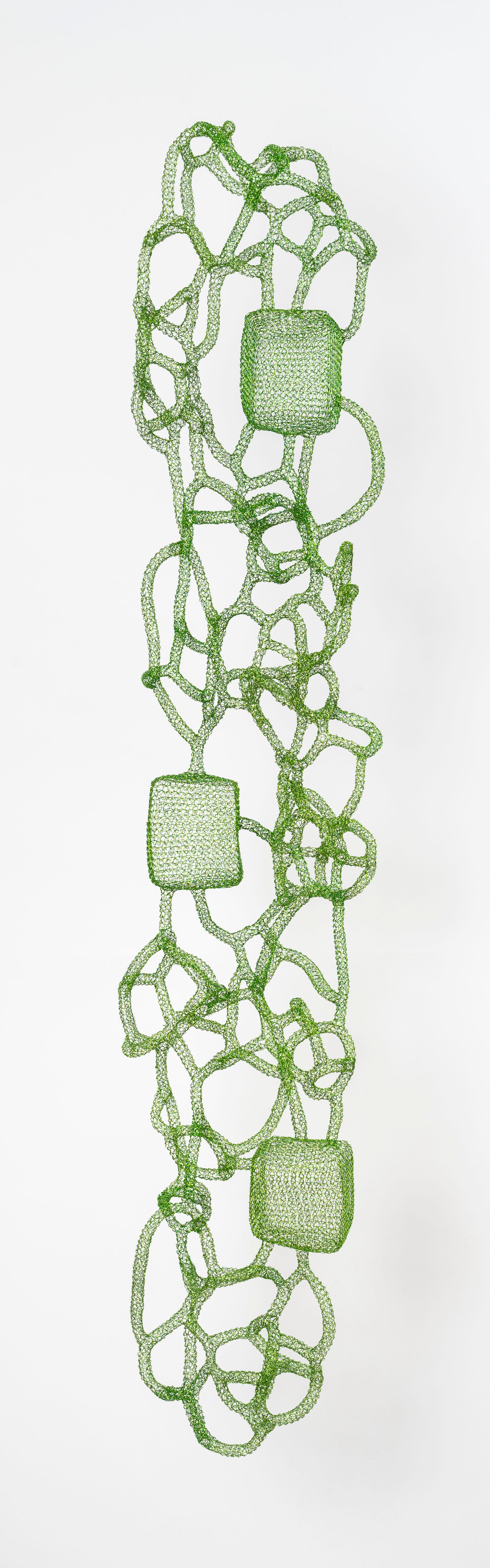 Named 'Fujino,' this metallic sculpture is hand-woven from lacquered green iron wire by the artist Delphine Grandvaux. Featuring cubic forms set within a complex web-like structure, it conveys a story of symbiosis between human achievements and