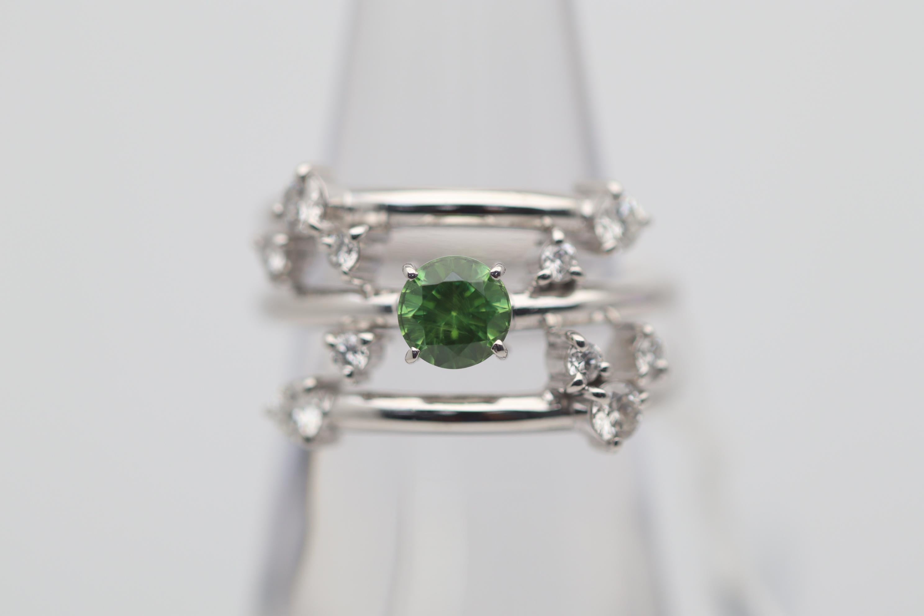 A fun and stylish spiral styled ring featuring a 0.66 carat demantoid garnet. It has a bright clean brilliant green color along with a classic horsetail inclusion confirming its Russian origin. It is accented by 10 round brilliant-cut diamonds set