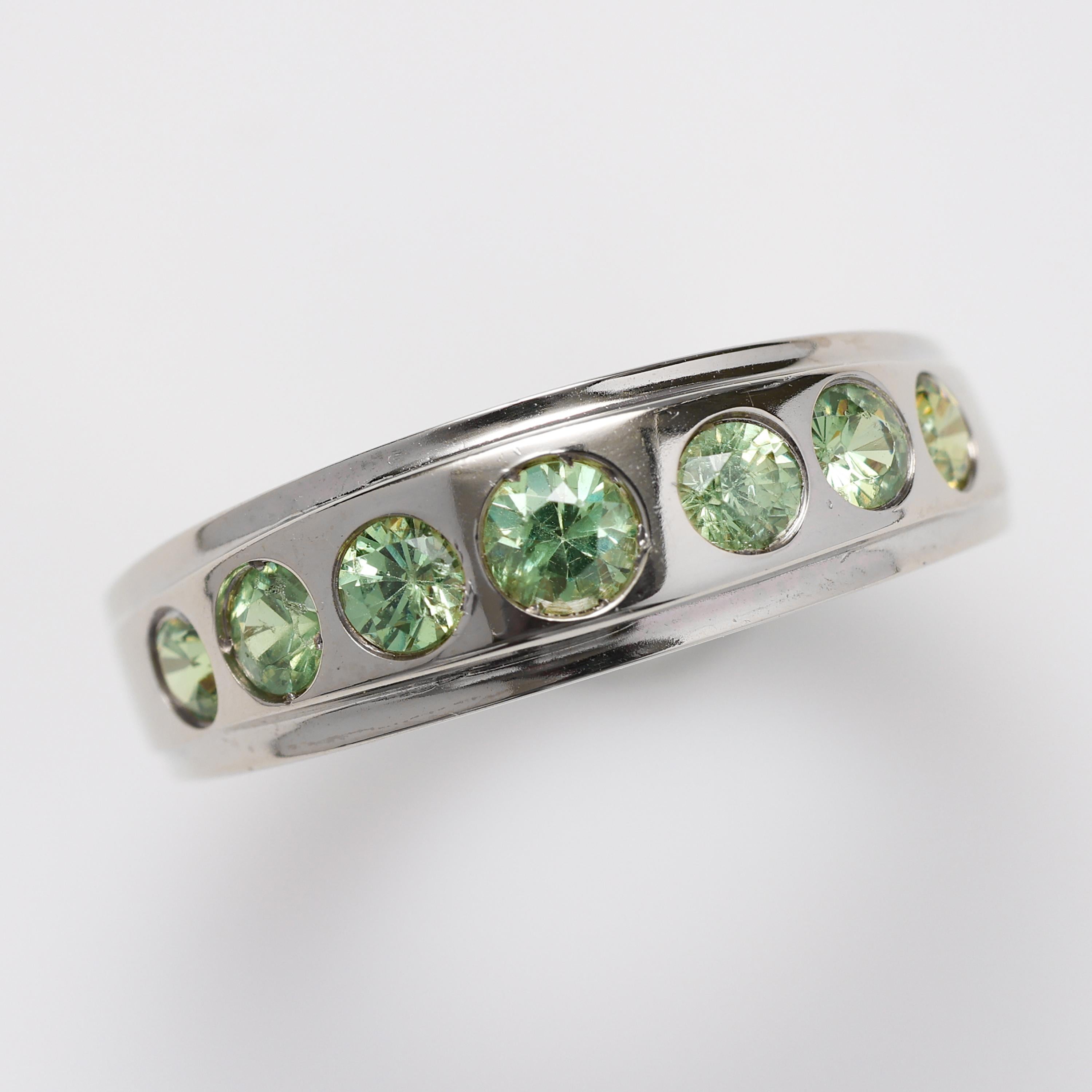 This sleek unisex 18K white gold ring features seven bright green demantoid garnets and would make the perfect wedding band or stack ring. Created by hand most likely in the late 1980s or early 1990s, this timeless classic is endlessly captivating