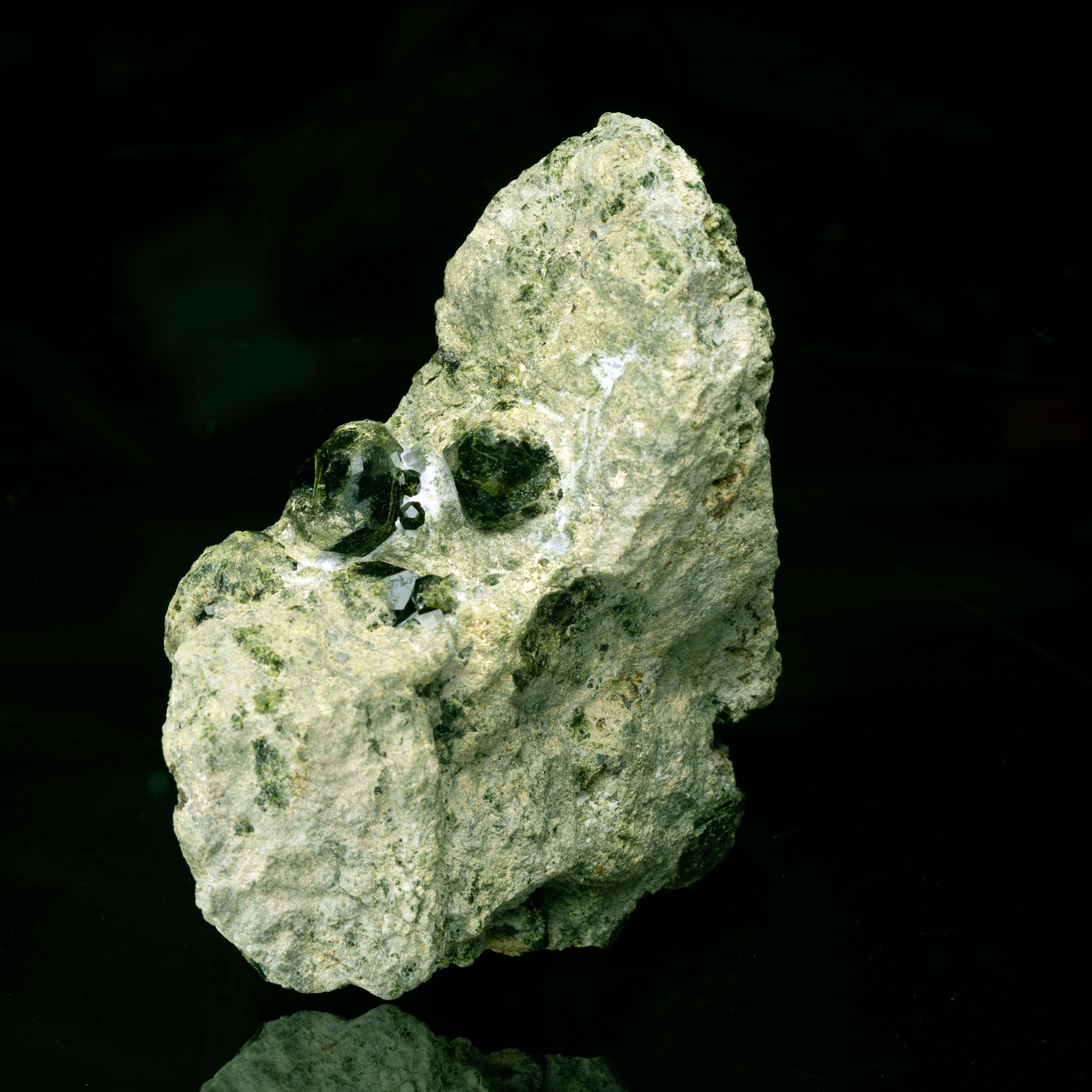 This show-stopping specimen features multiple sizable, intact, deep green demantoid garnets in various states of submersion within a rocky green matrix. The flat, earthy moss tone of the matrix plays brilliantly against the luster and fire of the