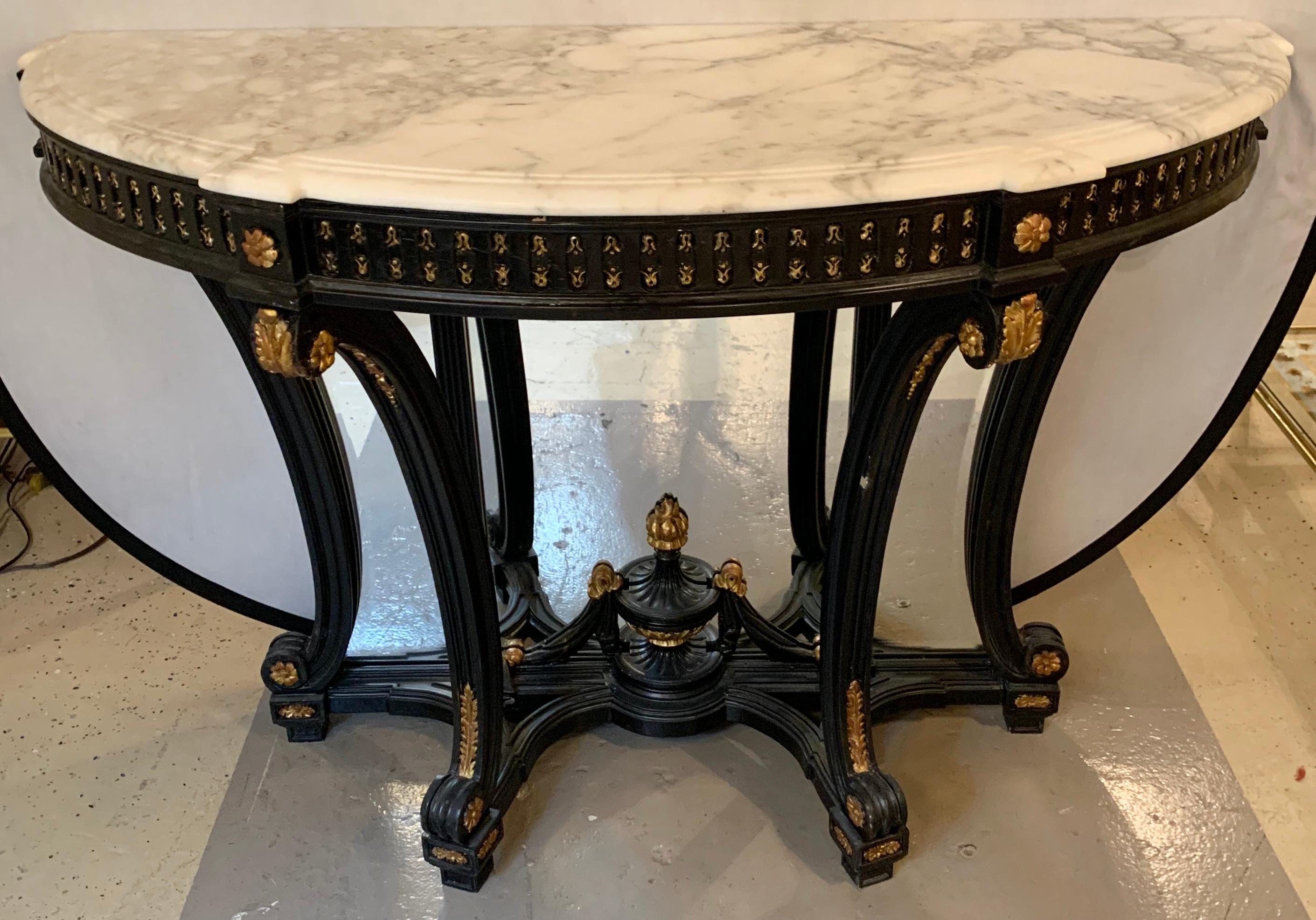 Demilune ebony and gilt Hollywood Regency style marble-top consoles or serving tables. A pair of fine custom quality parcel gilt and ebony decorated beveled mirror back console, serving or sofa tables. The pair with sprayed legs and a carved