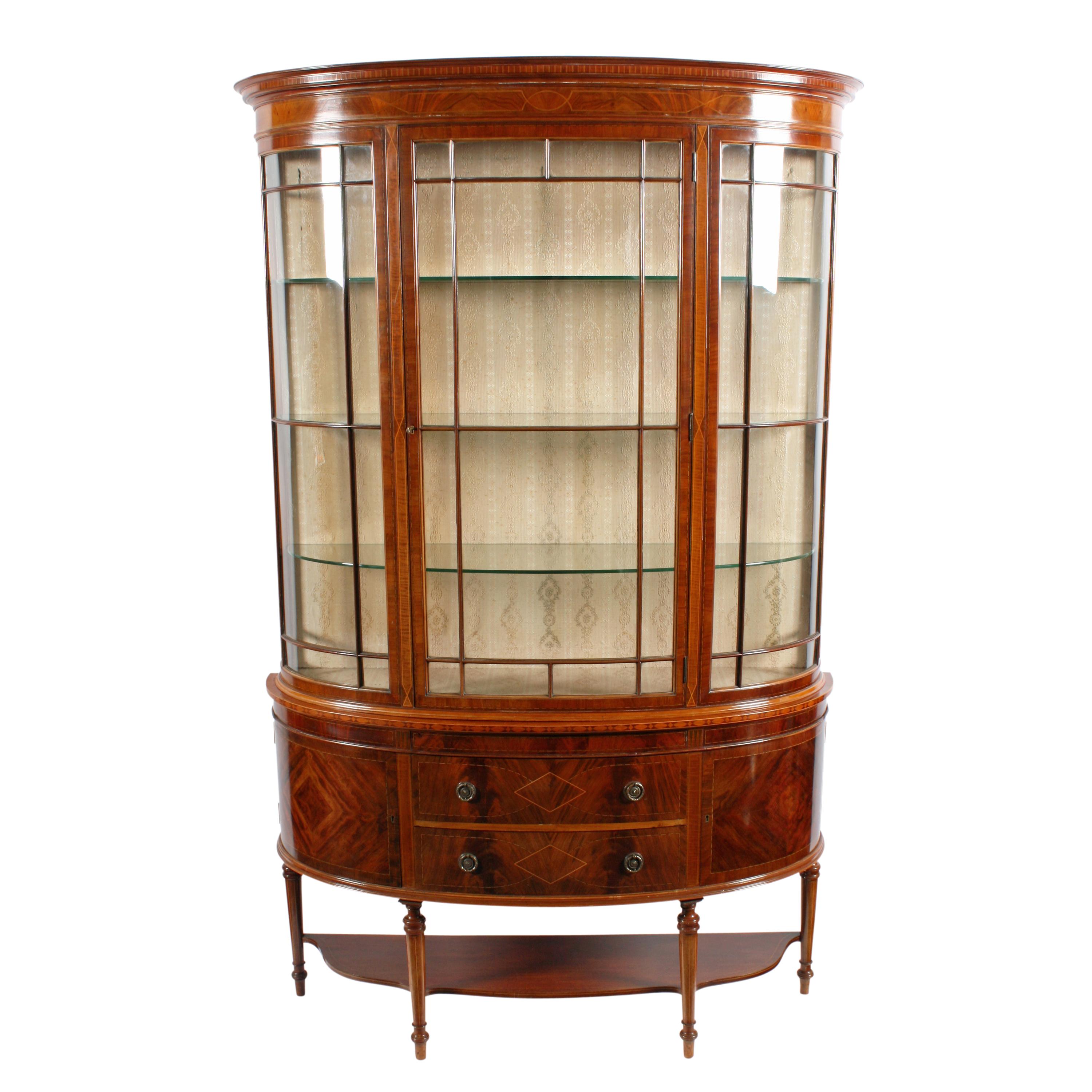 A fine quality Edwardian inlaid mahogany demilune display cabinet.

The cabinet has a central bow door with glazed bow side panels and three removable glass shelves.

The base has two mahogany lined drawers with brass ring handles and to either