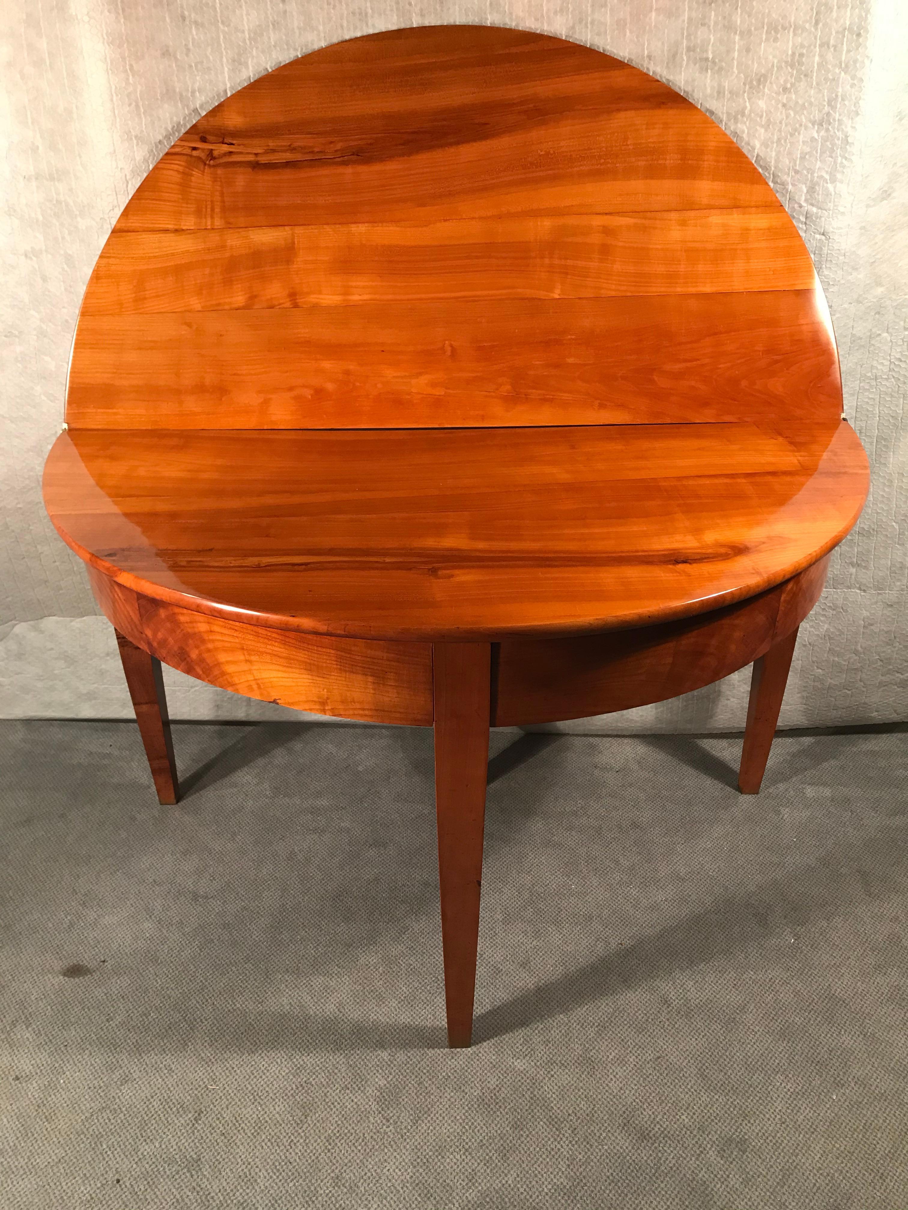 Exquisite demilune table, South German 1820, cherry veneer. The table can easily be used as side or console table. Additionally, you have the option to fold out the table top and use it as a dining table with a diameter of 49.21 inches (125cm). It