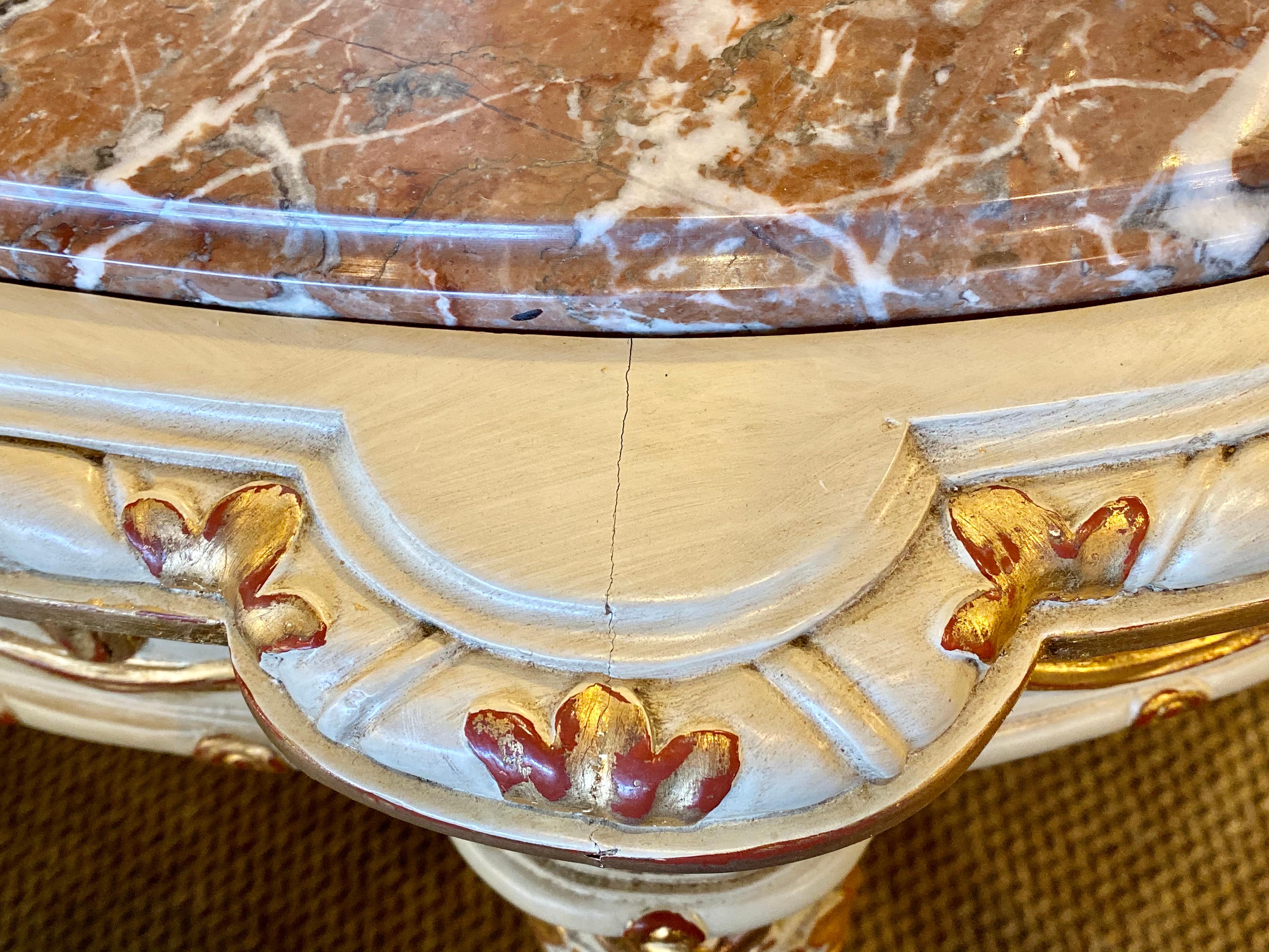 Maison Jansen console table having tastle and ribbon form with leaf design. This French console or serving table has a rouge and white veined marble top supported by a demilune shaped base that has been wonderfully parcel-gilt and paint decorated in