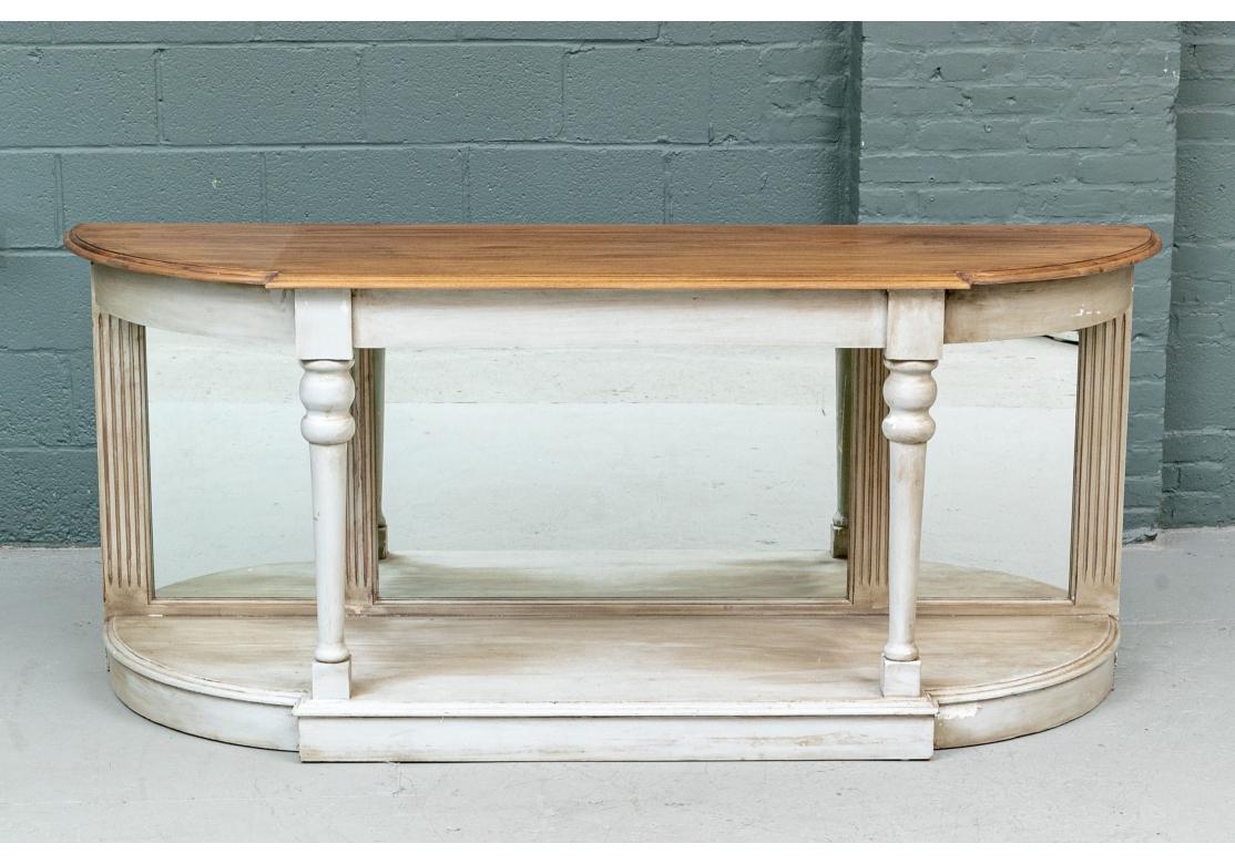 In an elegant stylized Neoclassical style with a shaped frame with carved edges. The plain pine top mounted on a greige painted frame, the lower tier in an antiqued painted finish. The back with fluted supports on the ends and between the triple