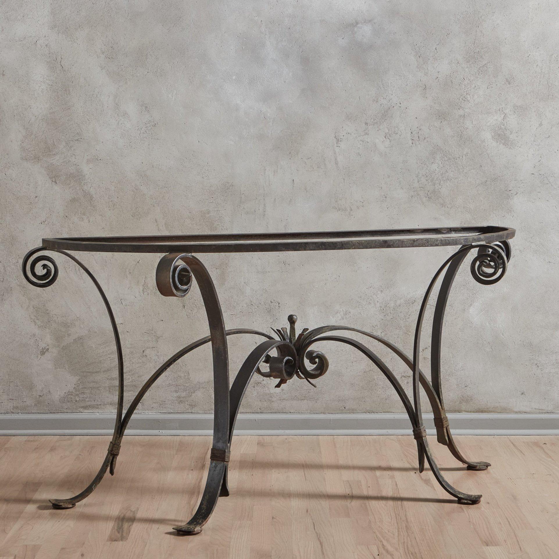 A 1940s French console table featuring an intricate wrought iron base with scroll motifs and a decorative central finial, which is supported by four curved support bars. This table has a new 1” thick honed green demilune soapstone table top with