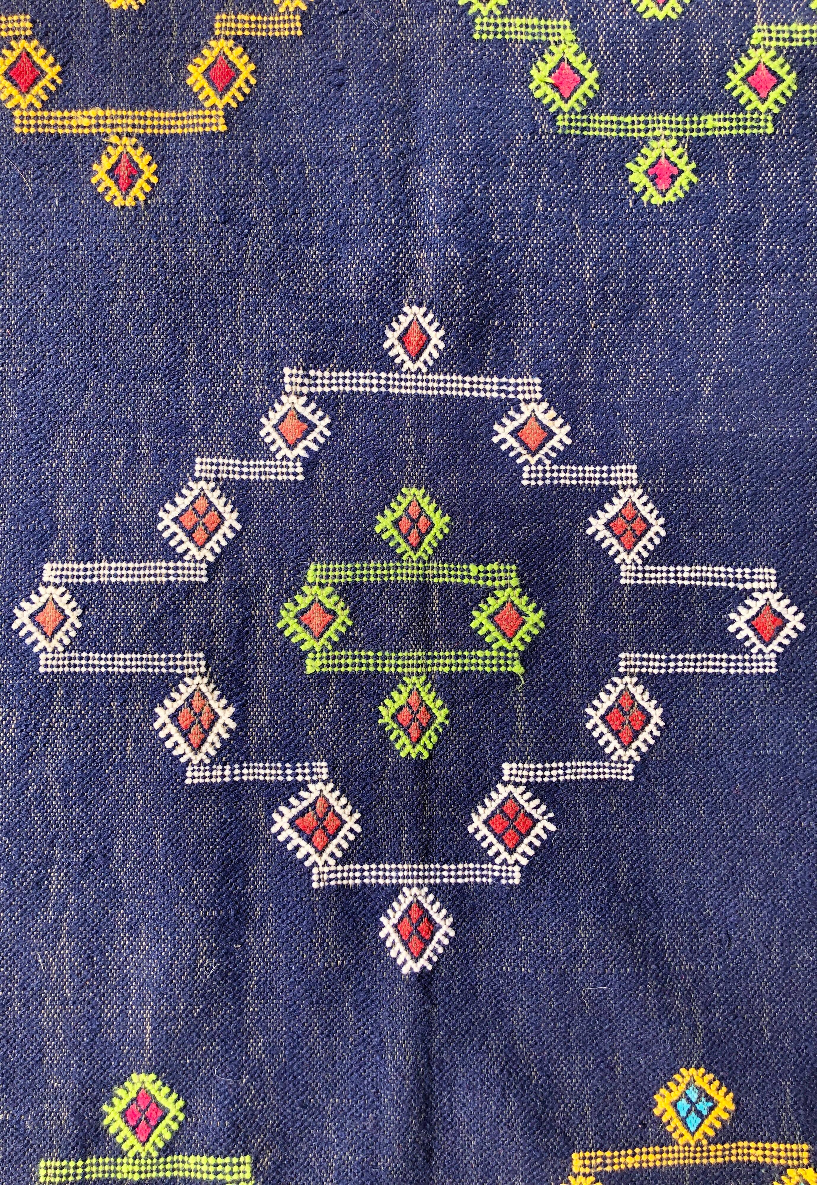 This durable Moroccan blue throw rug features tribal designs in handspun cotton yarn. The diamond shapes are indicative of the evil eye, with the rug offering protection from ill will. Sourced directly from a women's cooperative in Tansikht,