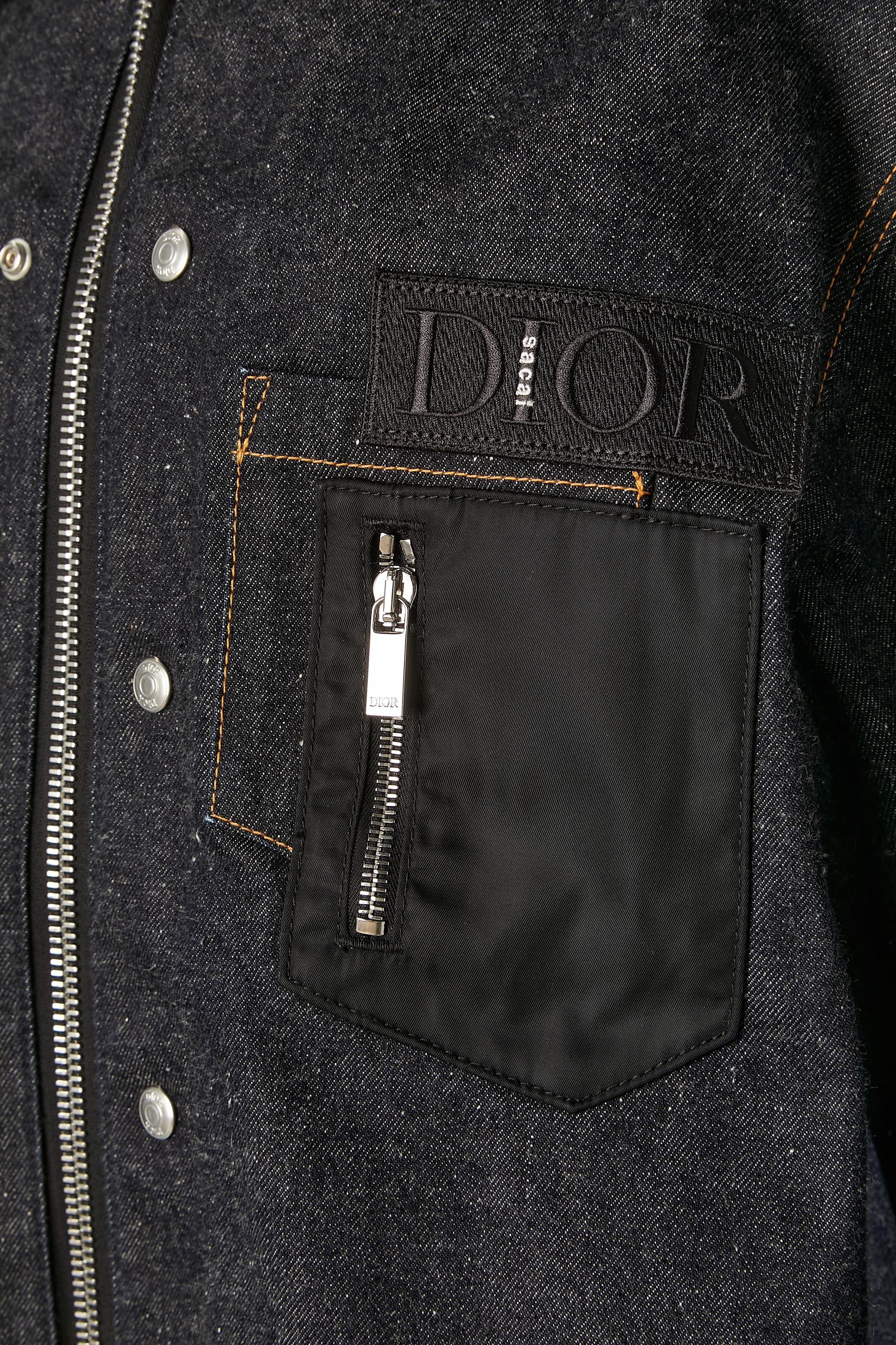 Veste en denim avec détails en nylon noir. Fermeture zippée sur le milieu du devant + bouton pression décoratif 
 Fendu des deux côtés avec fermeture à bouton-pression. Une poche extérieure sur le devant et une poche intérieure. Fermeture par