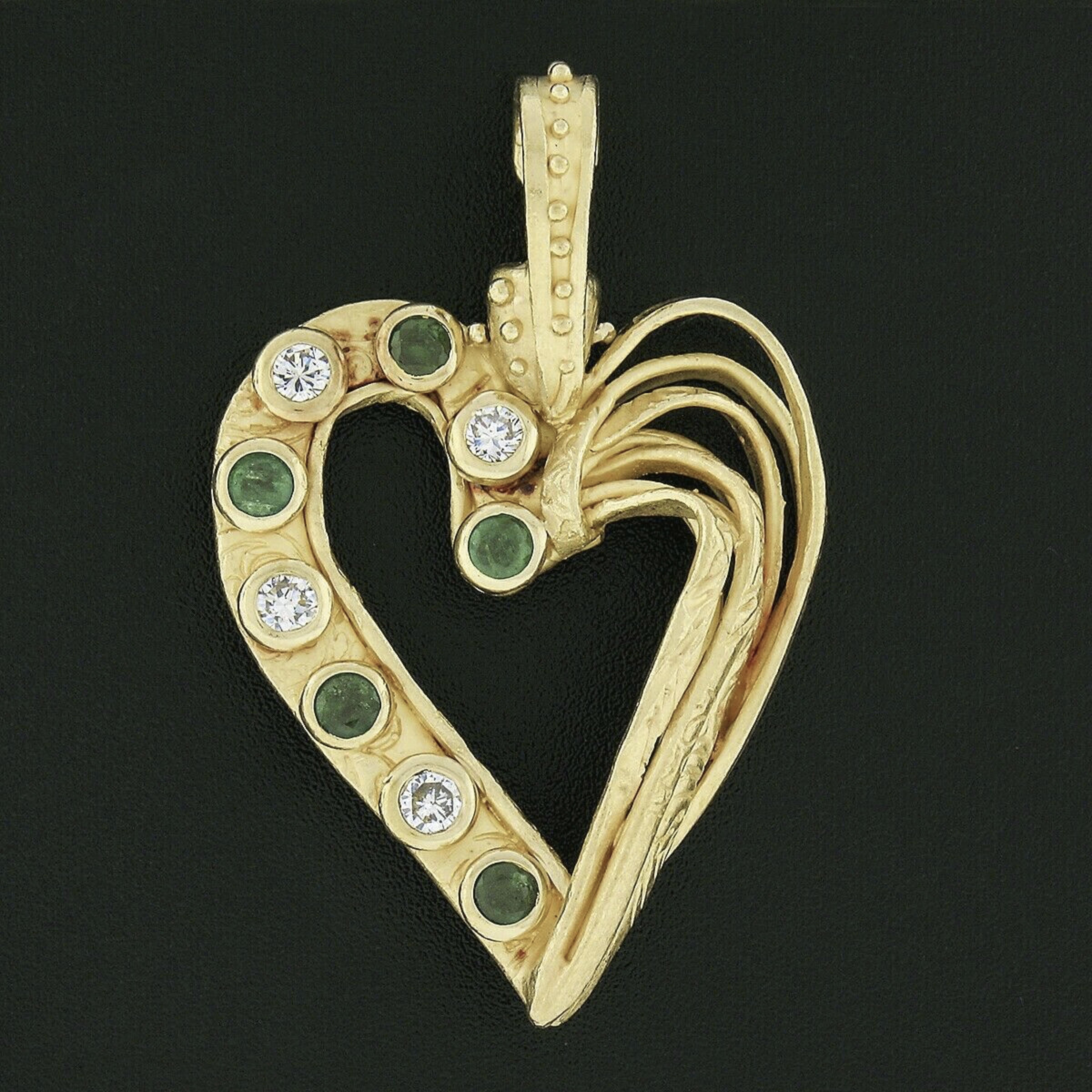 Here we have a magnificent open heart statement pendant designed by Denise Roberge that is crafted in solid 22k yellow gold. This large pendant features approximately 1.08 carats of fine quality emeralds and diamonds that are neatly bezel set at one
