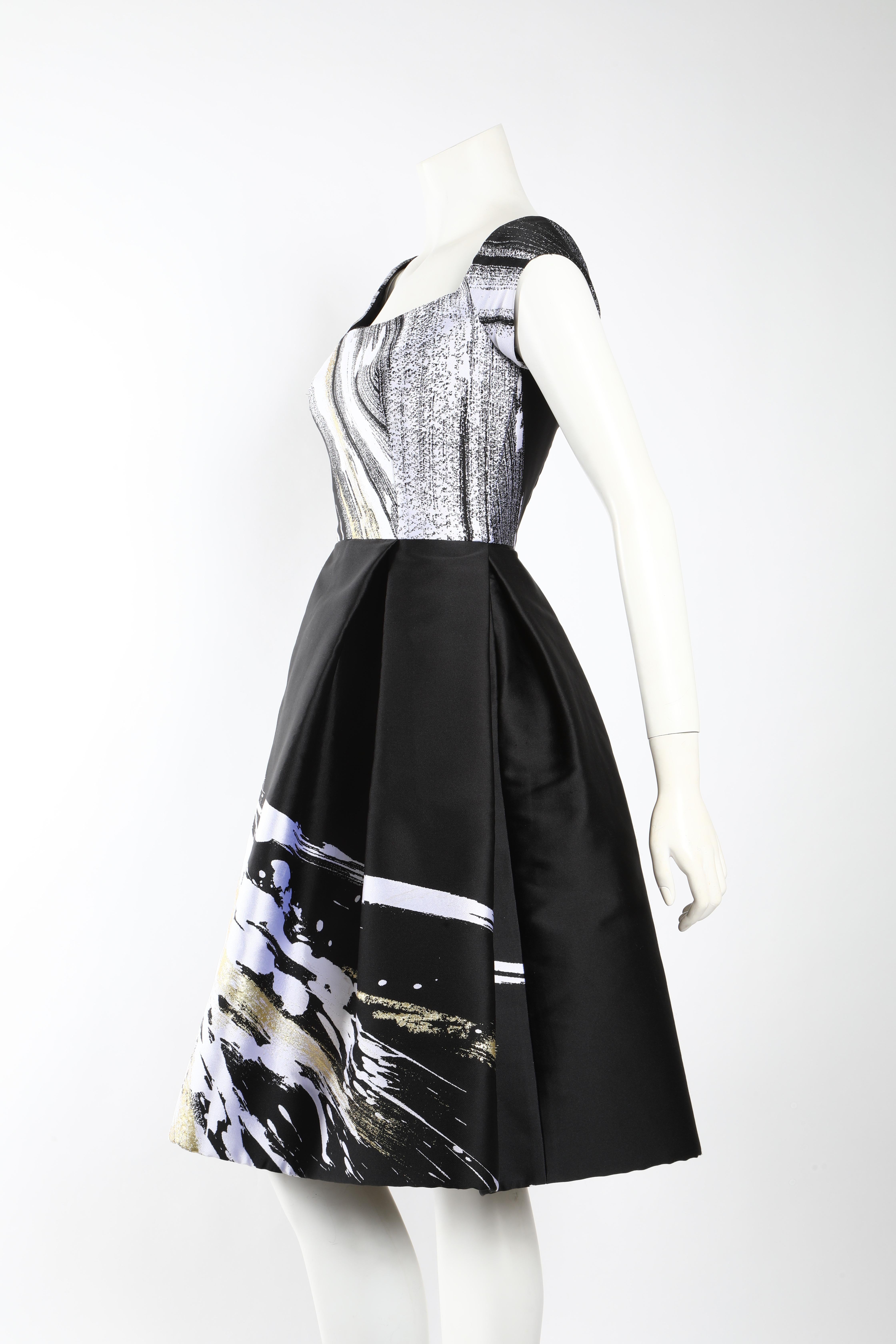 Cocktail dress by Dennis Basso in black and white adorned with a whimsical splash of gold. Features a boat neck and cap sleeves. Fitted through the bodice with a full skirt that hits at the knee. Boning in the bodice creates structured shape, which