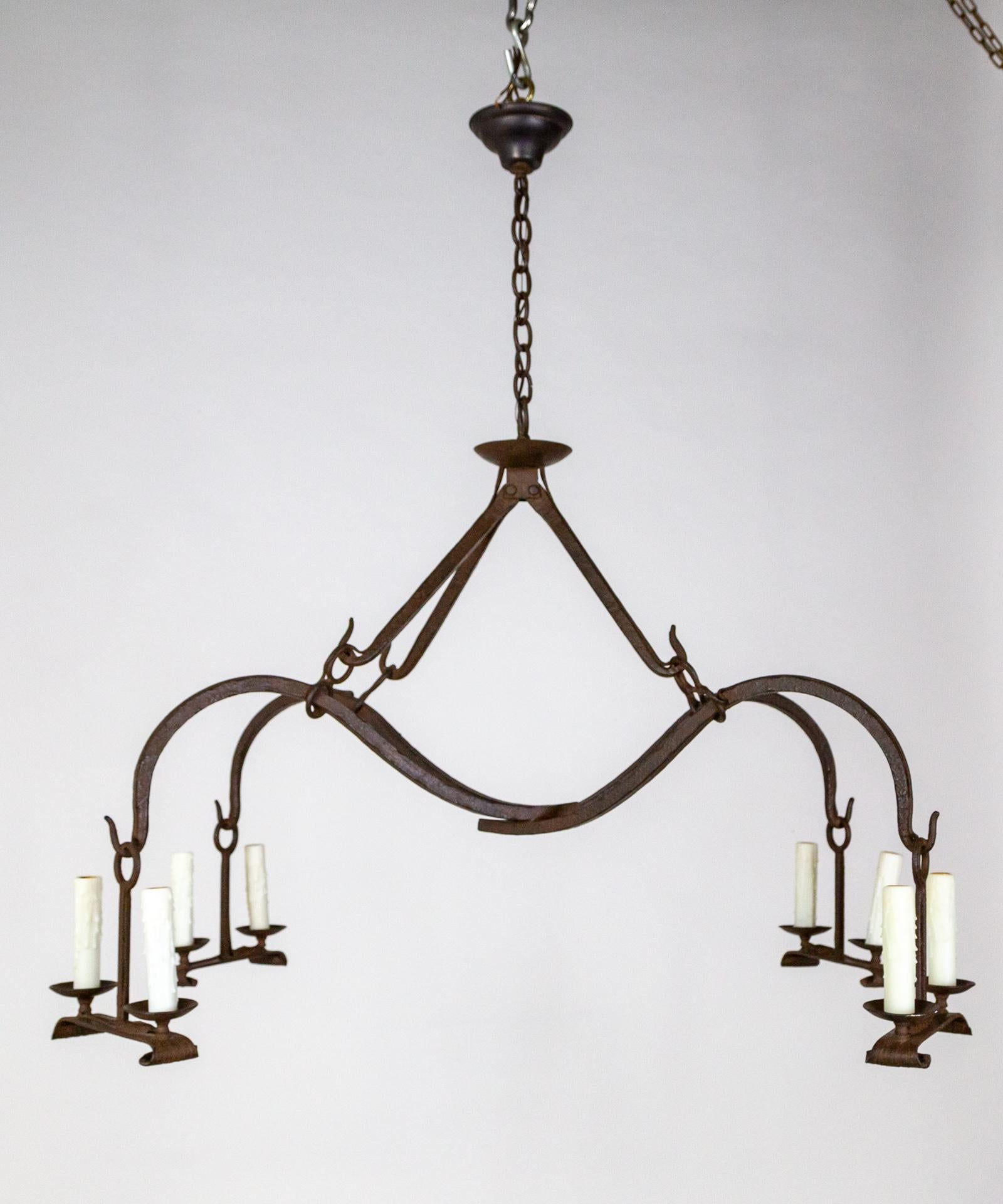 A uniquely shaped iron chandelier with criss-crossed, swooping arms and four hanging twin candle style lights. A powerful modern Gothic design with a spacious feel by Dennis and Leen with hammered hook details in a black finish. 21st century. Takes