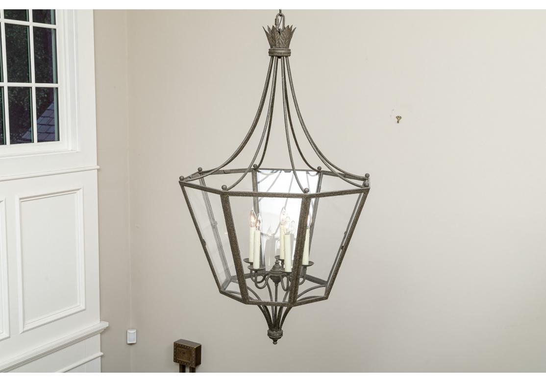 Neoclassical style patinated lantern with eight glass panels and three illuminating wax candle style lights. The large fixture with 8 curved rods emitting from a feathered corona and conjoined with 8 framed and beaded glass panels and terminating