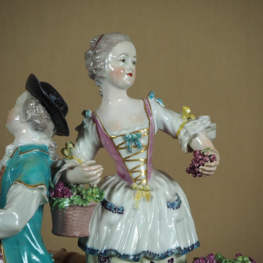 Handsome Derby group of Vignerons, with a colourful man & lady standing on a rocky plinth, he with a barrel and cup, she with two baskets of grapes and in the act of picking more, with gilt rococo moulding to the rim. 

Unmarked, with 'patch
