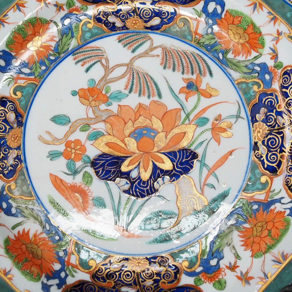 Derby octagonal plate, from the Lowther Castle service, richly decorated with an Imari pattern consisting of a central orange, green, blue and gilt water lily and flowering trees, flanked by borders of intricately gilt blue clouds and panels of