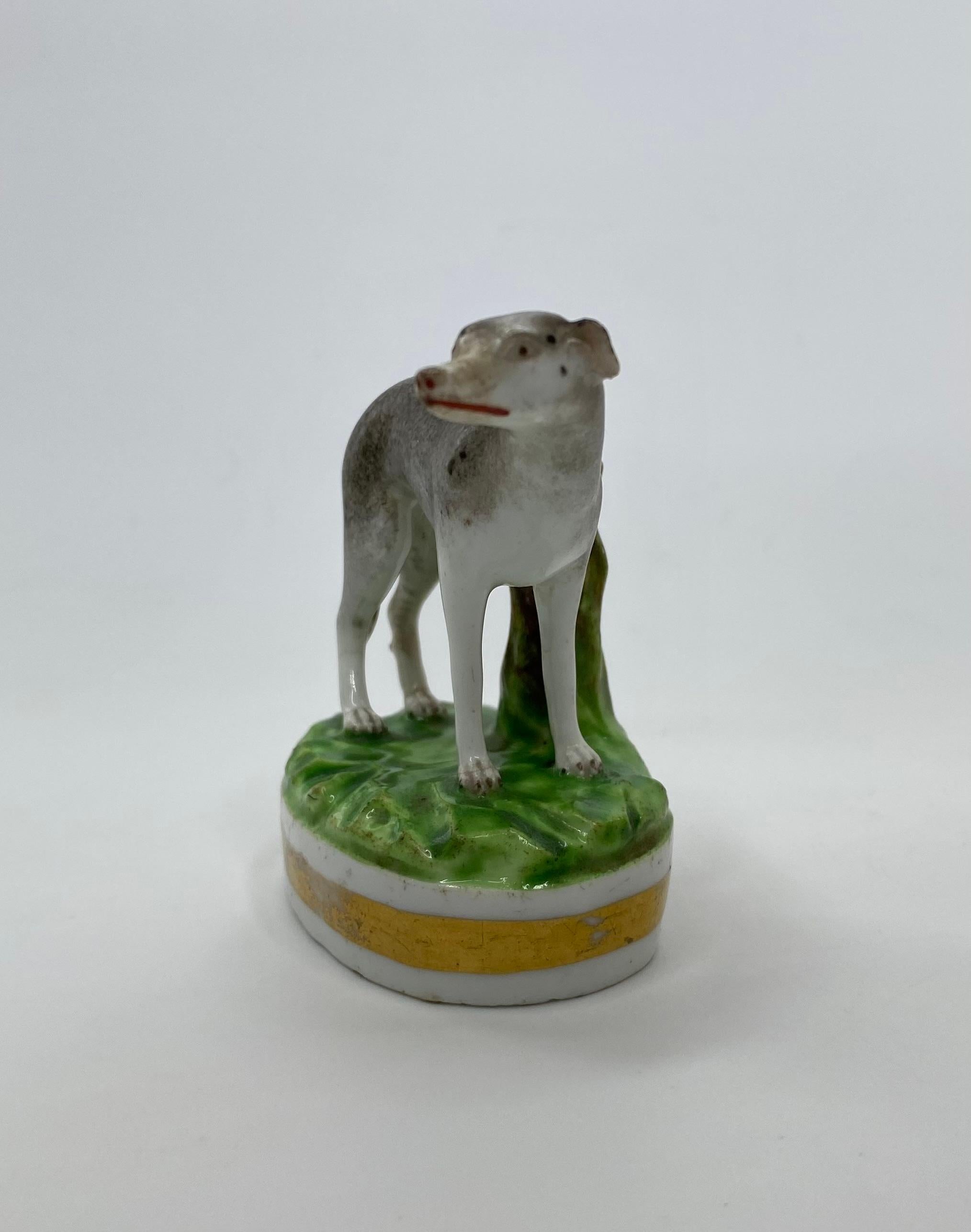 A rare and charming Derby porcelain Greyhound, c.1830. The beautifully observed Greyhound, hand painted in grey, with black markings, standing before a tree stump, upon a grassy mound base.
Having a broad gilt band to the oval base.
Printed Derby