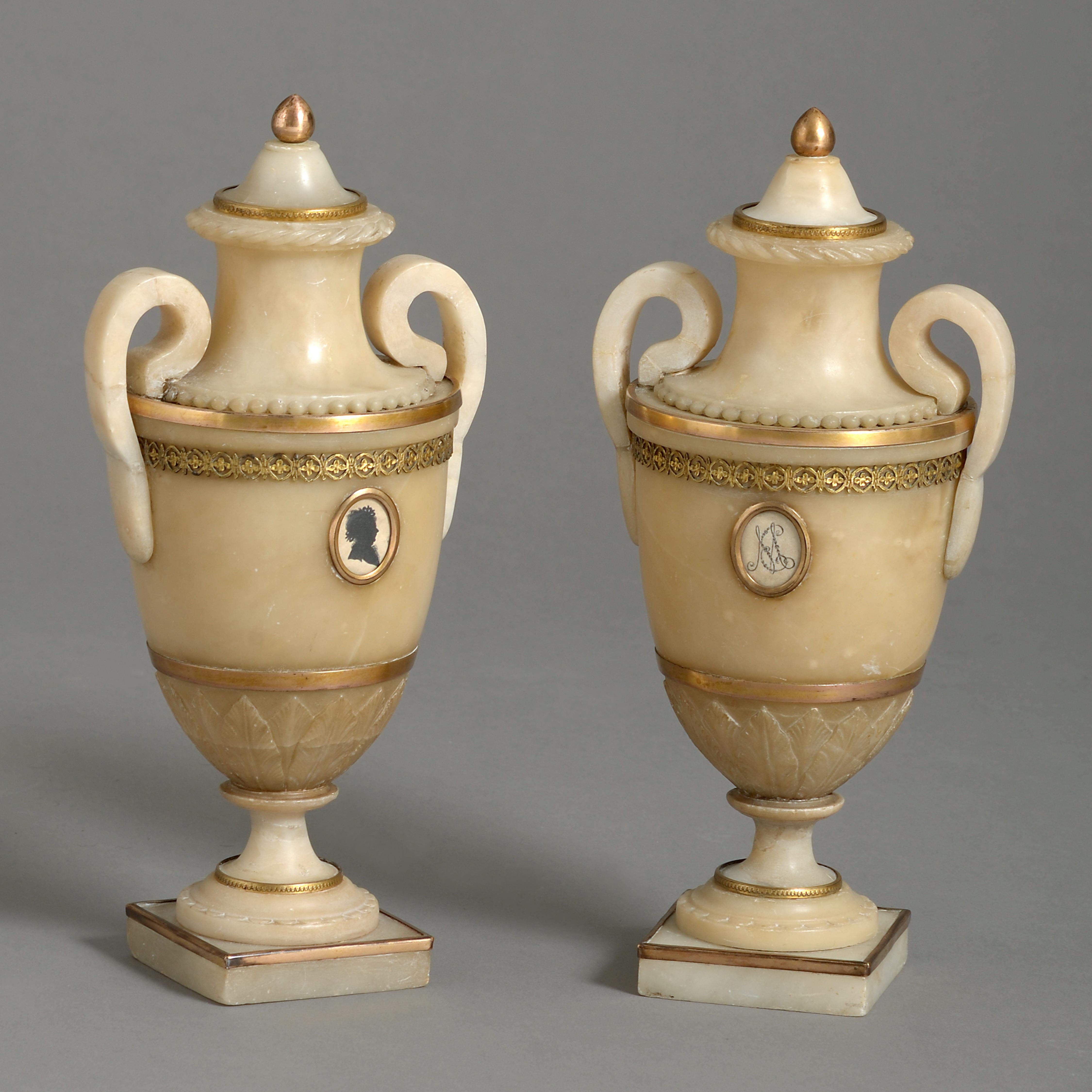 A fine pair of George III Ormolu-mounted Derbyshire alabaster urns, circa 1780.
Each with a glazed oval plaque, one containing a silhouette, the other with a cypher. Restorations to the socles and handles.