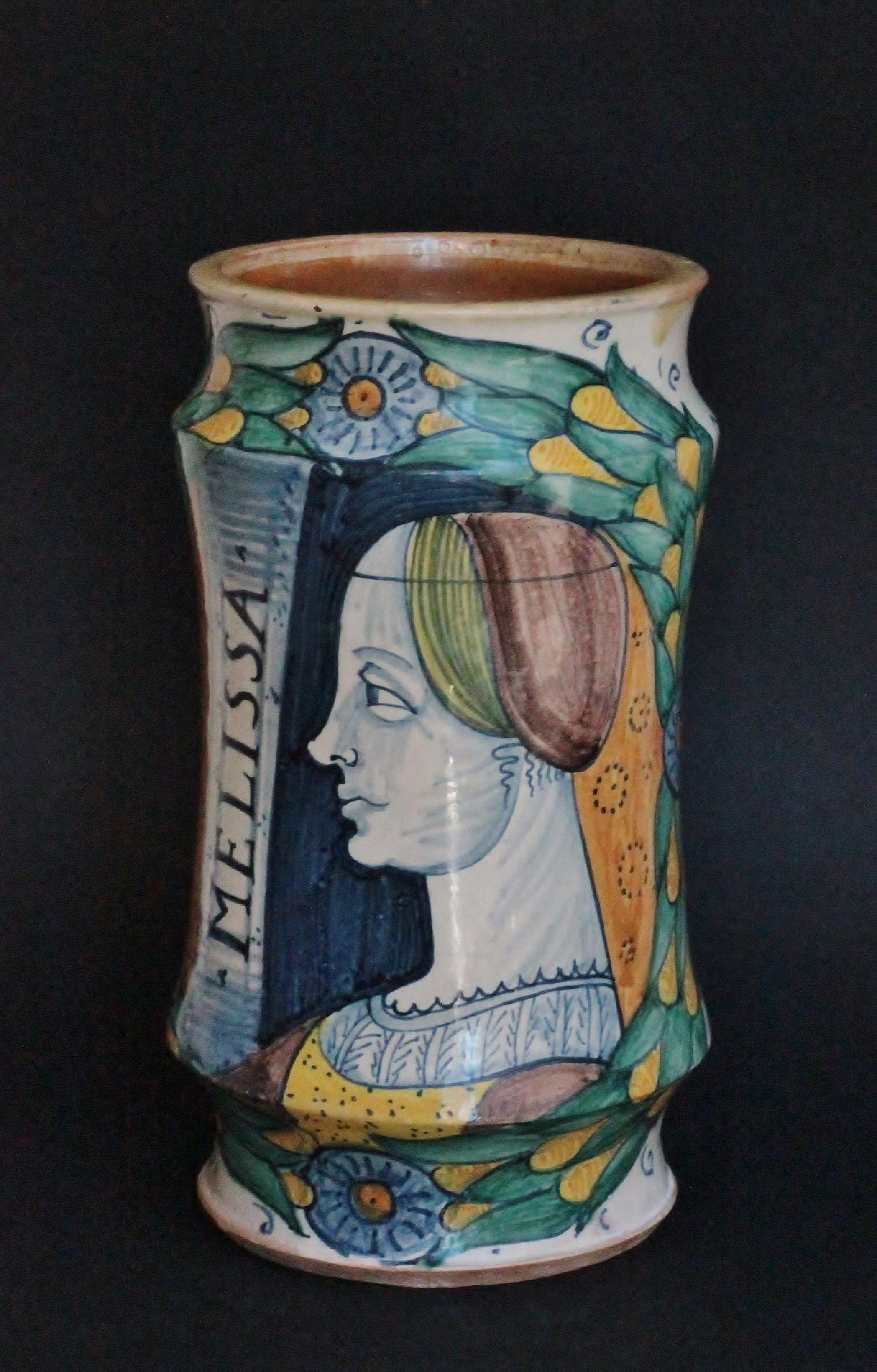 An apothecary albarello of cylindrical form in majolica of Deruta with a ‘Bella Donna’ type painted in blue, yellow, ochre and manganese: a bust of a lady in profile to the left with an inscription: “Melissa”, a scroll foliage with flower
