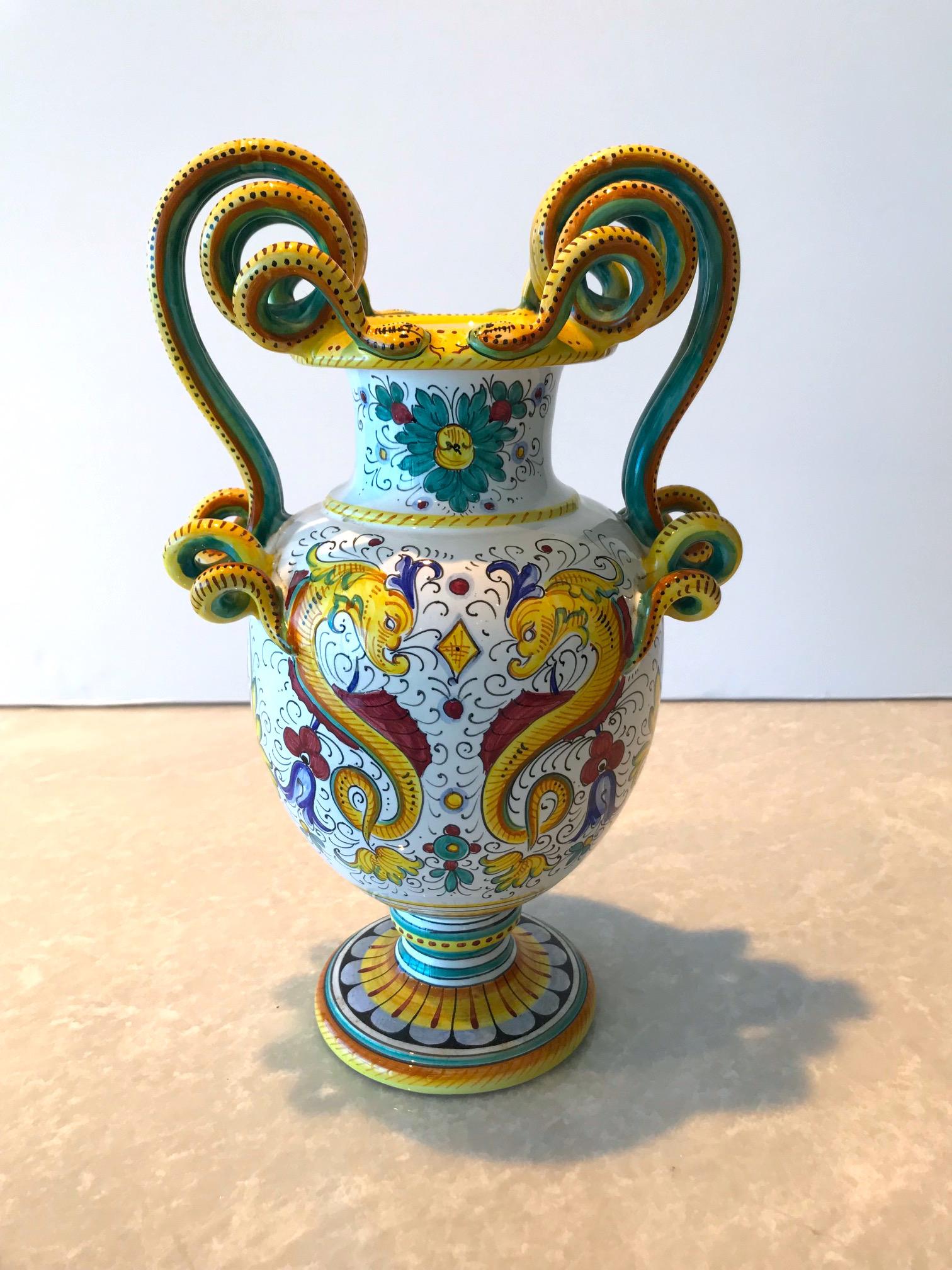 Exquisite Majolica vase with hand painted tin glaze over earthenware ceramic pottery. Handmade with stylized serpentine handles and elaborate painted designs throughout including the iconic dragons. Vase has pedestal base design and has vibrant hues