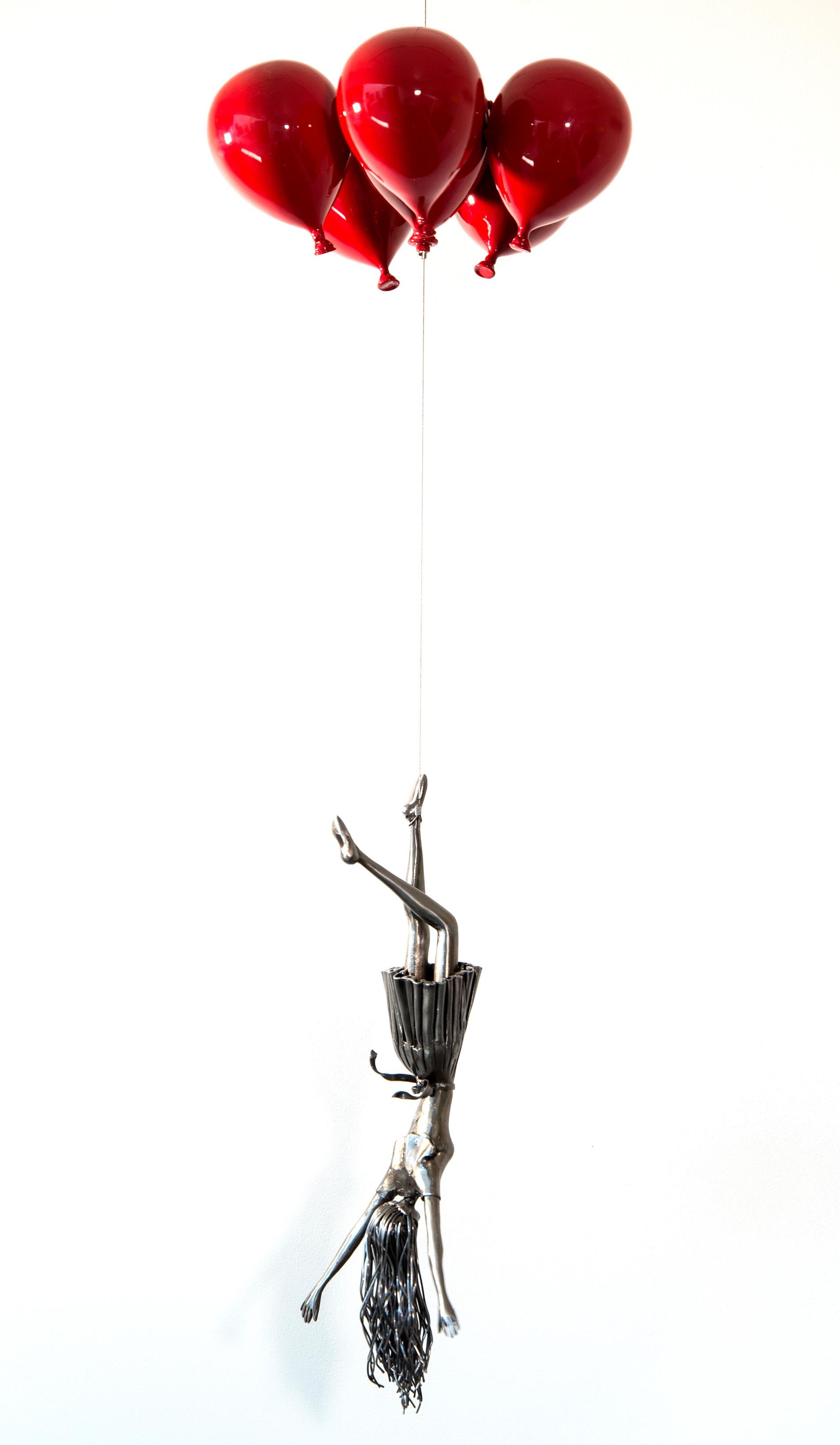 In this piece, Derya Ozparlak’s stunning steel figure of a woman hangs upside down, her long hair trailing behind her as she’s carried away by a bouquet of shiny red balloons. 
Ozparlak’s metal sculptures are intended as a metaphor for the angst of