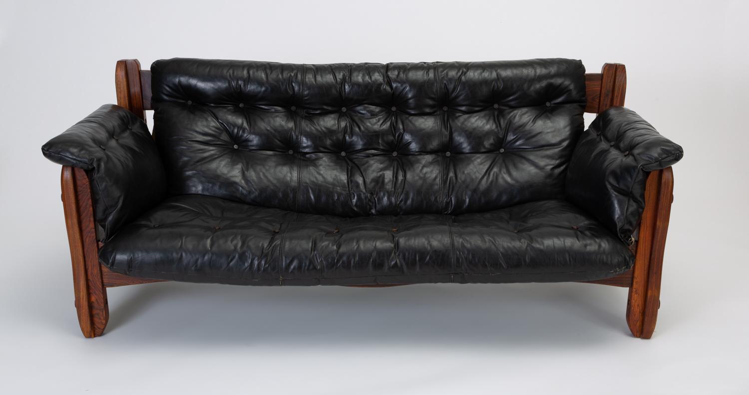 A deep sofa from Don Shoemaker’s “Descanso” line produced in highly figured cueramo wood and black leather. The blocky construction and broad planes of the frame showcase the almost marbled appearance of the woodgrain, while the wavy edges and