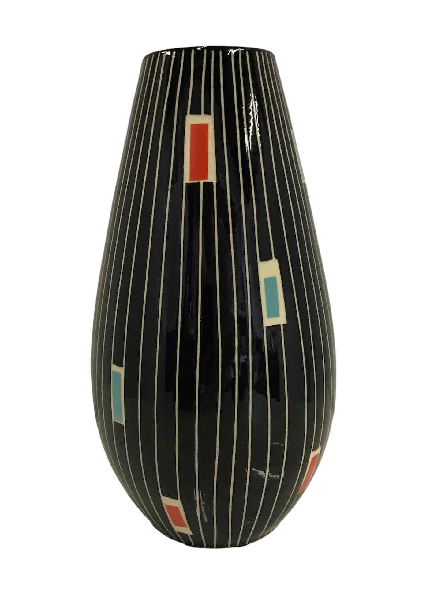 Eine Reihe von farbigen Rechtecken auf senkrecht eingeschnittenen weißen Linien über einem
schwarzer, glänzender Glasurhintergrund definiert diese Midcentury Modern Vase von
Üebelacker-Keramik auch bekannt als Ü-Keramik von Deutschland. Das