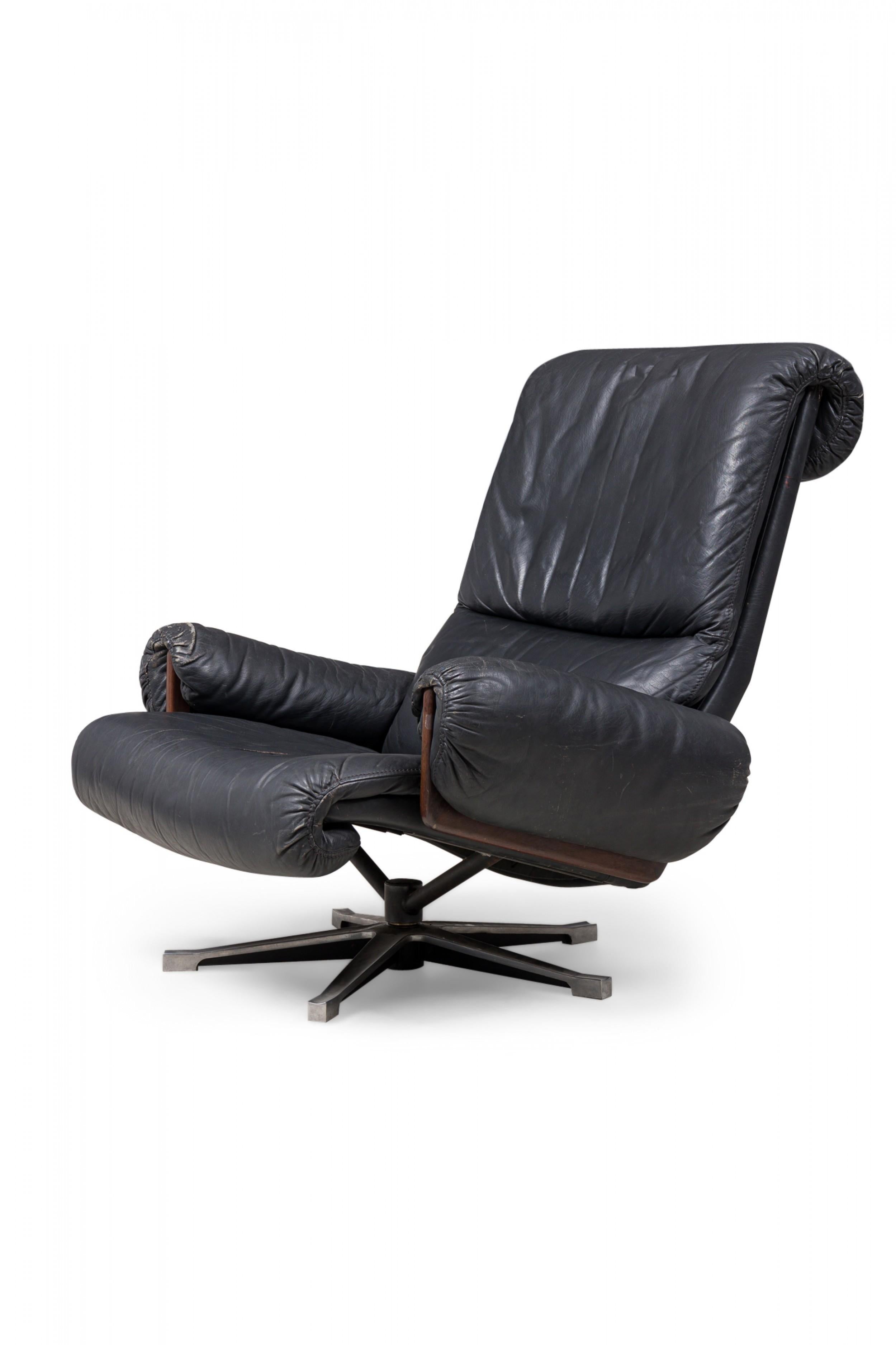 midcentury Swiss (1970s) metal swivel chair with incurved back, seat and arms upholstered in black leather, supported by a star shaped, swivel base with small circular adjustable feet. (Matching ottoman: REG5054) (De Sede).
