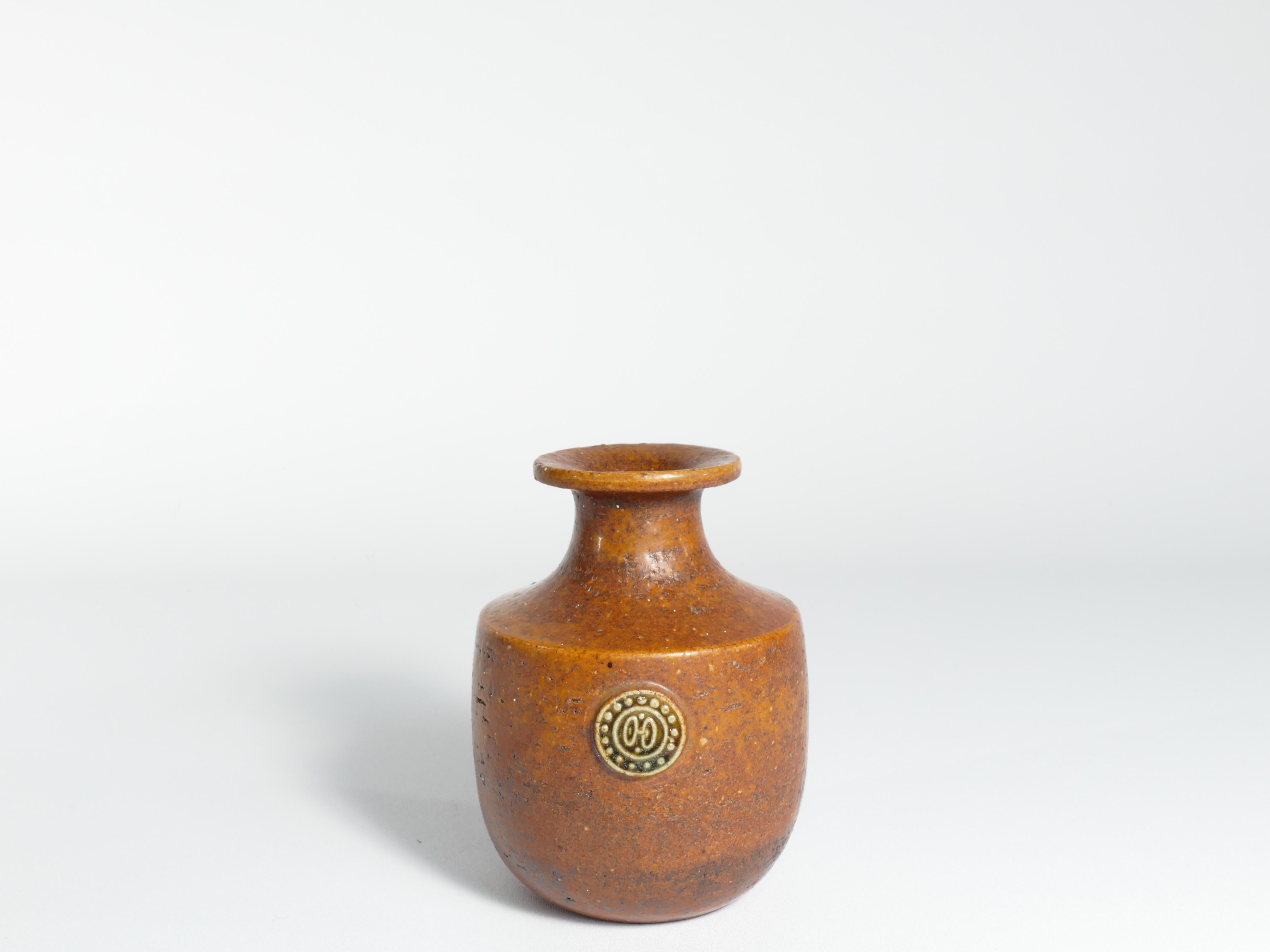 Le vase de Sven Wejsfelt présente une forme robuste et terreuse, ornée d'une riche glaçure brune et d'un cachet en relief complexe. Cette création en forme de chamotte date des années 1970 et constitue un ajout notable à la série Sahara. Véritable