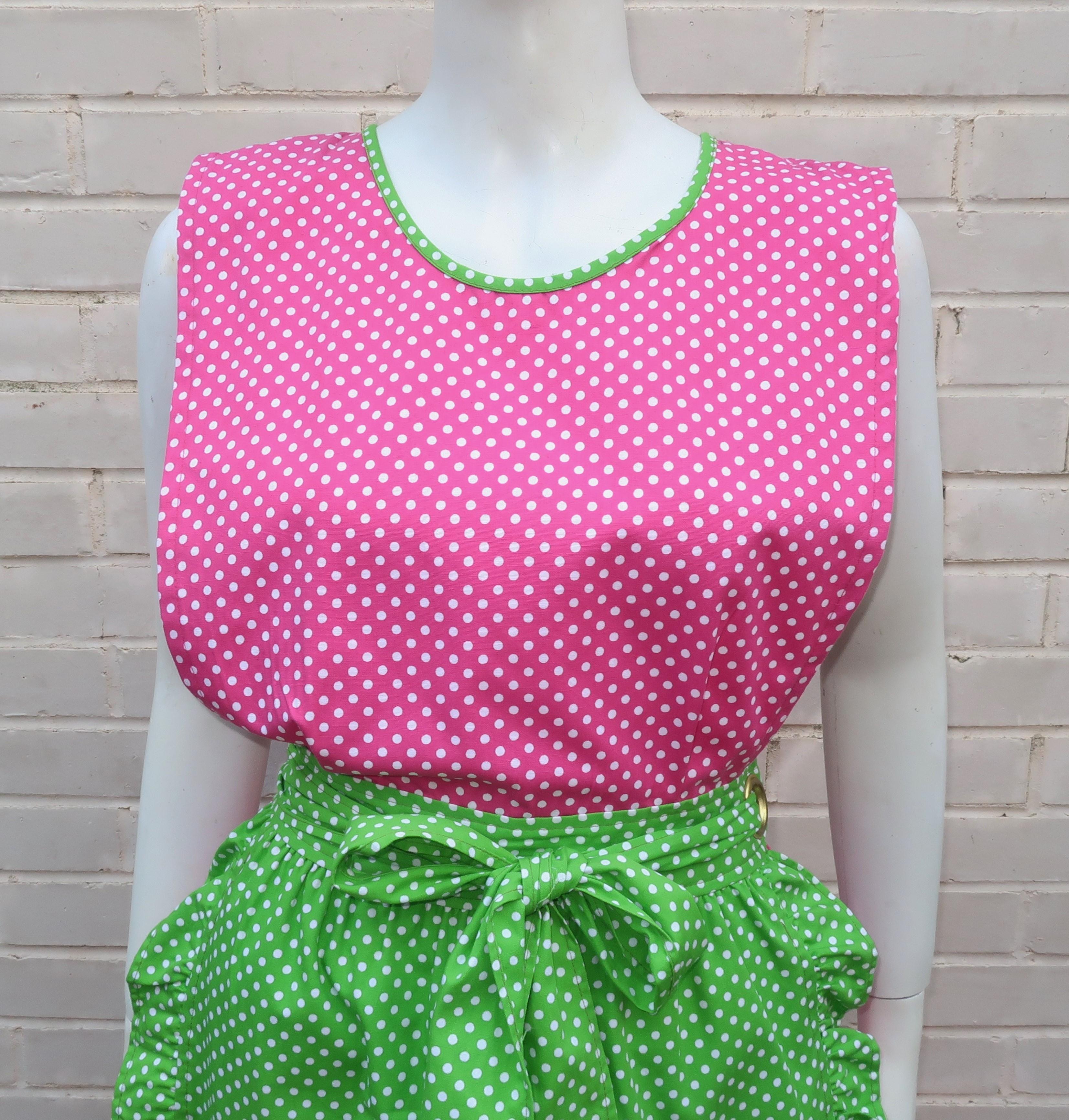 C.1970 pink and green polka dot cotton dress by Design House of Japan.  The maxi dress has a pinafore construction with ties that criss-cross at the back and feed through a large gold tone metal grommet on the side for a wrap effect.  The dress also