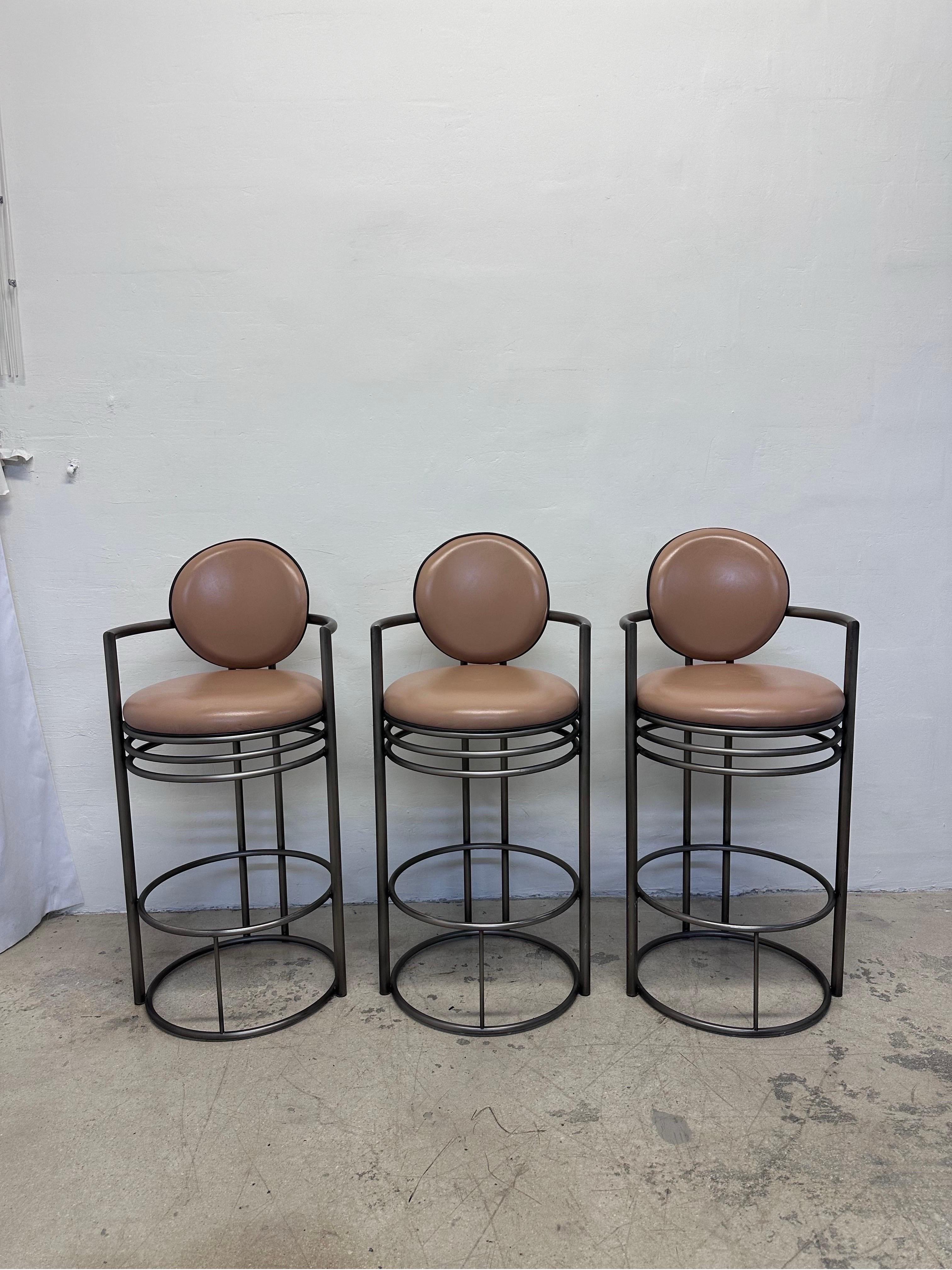Set of three Art Deco revival modern bar stools with nude leather cushioned seats and back rest with black piping on a tubular steel base.  Designed and manufactured by DIA - Design Institute America circa 1980s.

Arm Height: 34-3/4