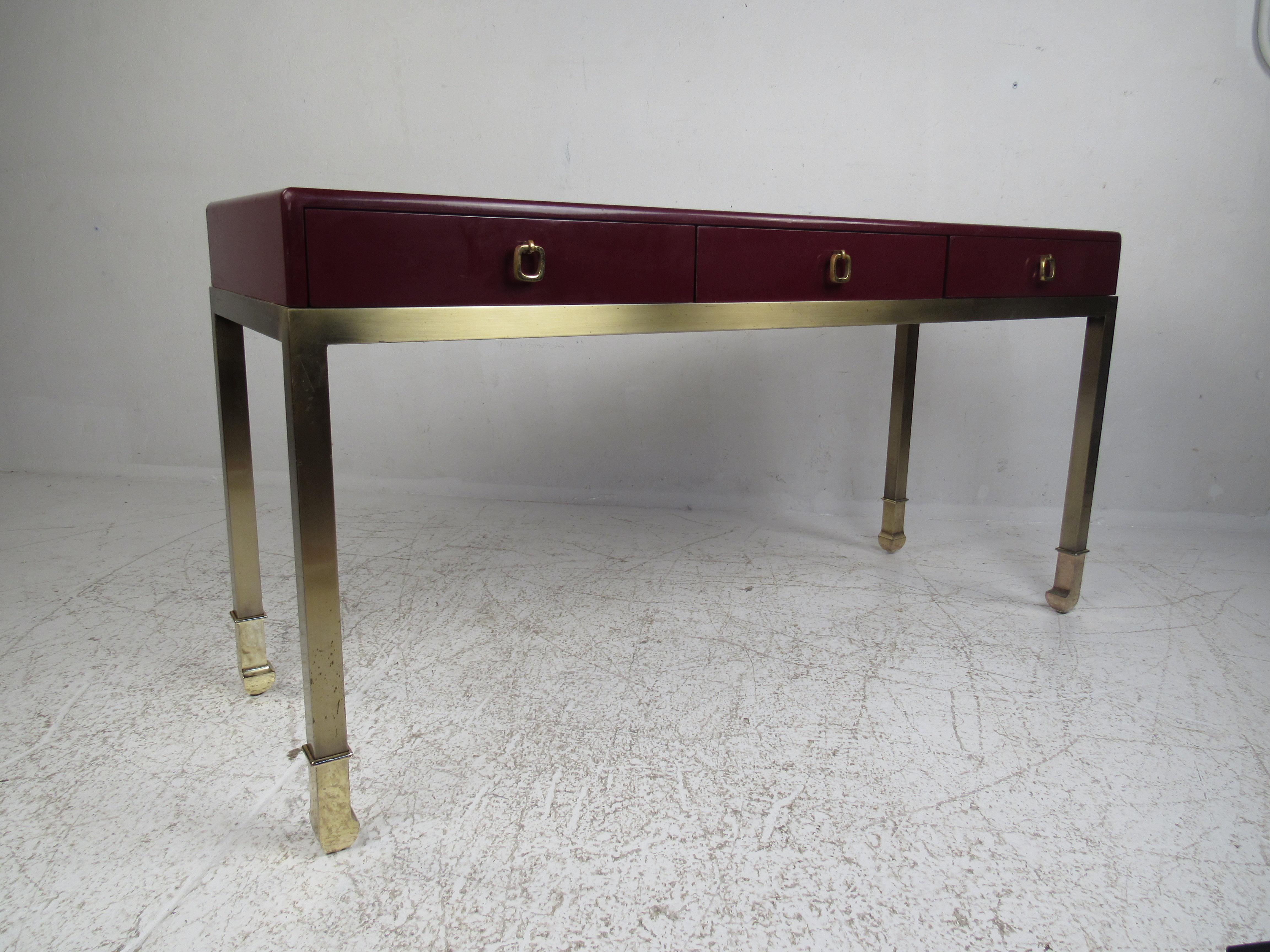 An elegant vintage modern maroon colored console table with unique brass drawer pulls and sculpted feet. The three hefty drawers ensure plenty of room for storage. This versatile Mid-Century Modern piece functions as a desk, vanity, or hall table. A