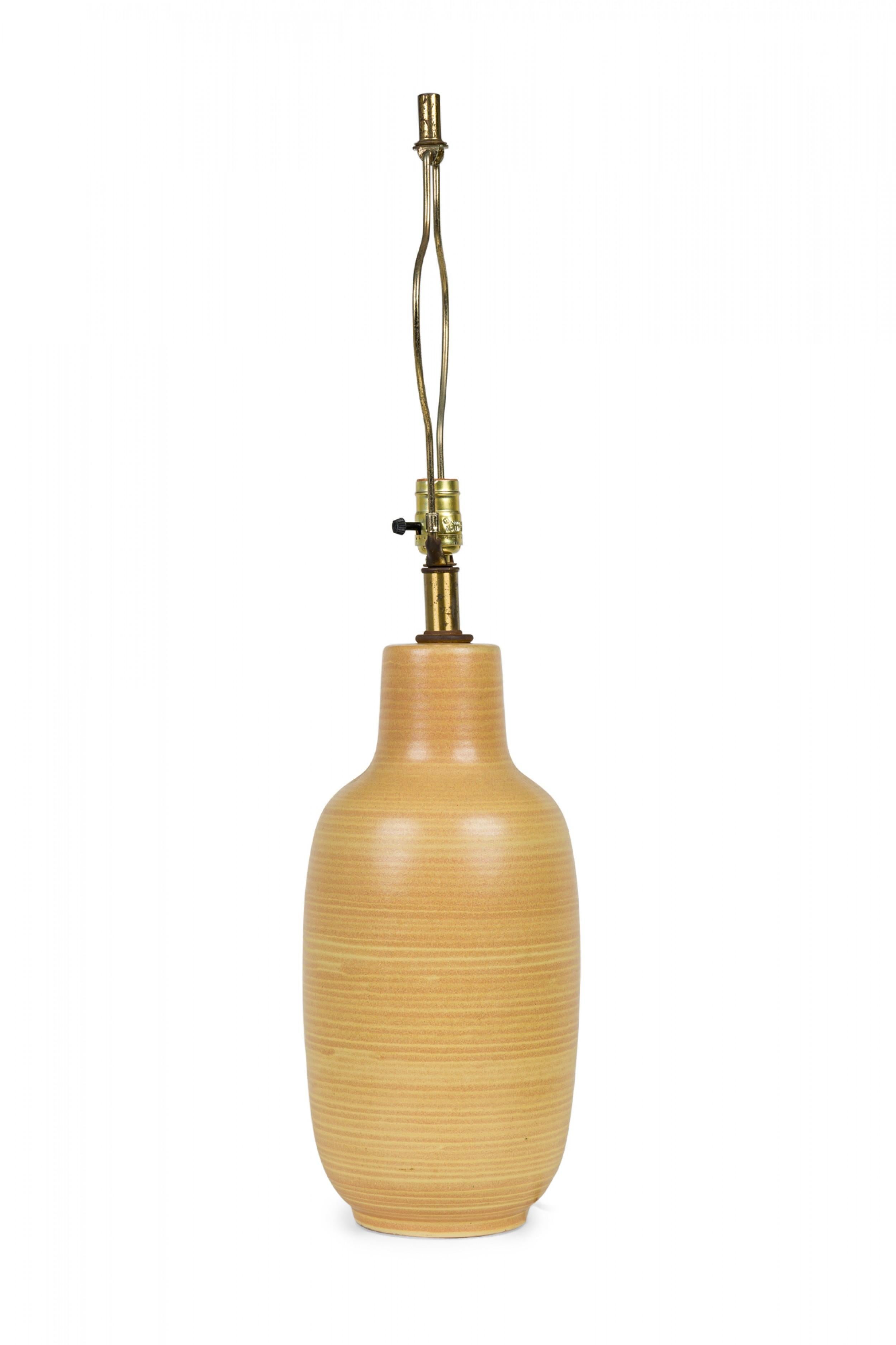 Mid-Century American ceramic table lamp in footed bottle form with an extended brass stem, harp, cylindrical finial and functional light switch socket, fired in a mustard striped matte glaze. (DESIGN TECHNICS)

32.5