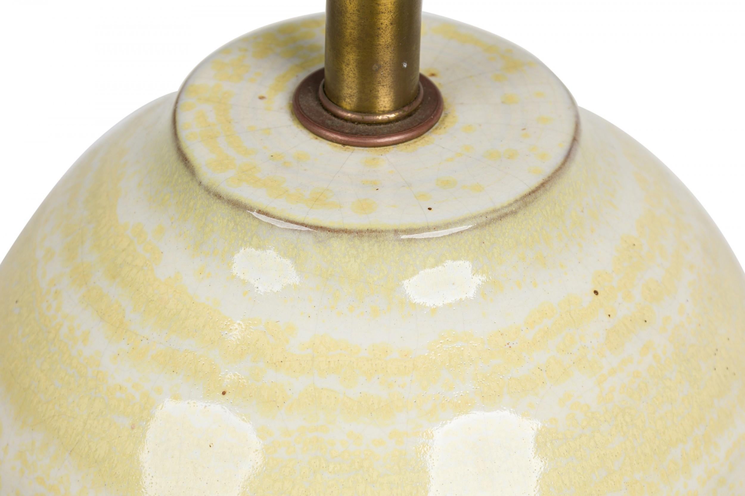 Mid-Century American ceramic table lamp in flared ovoid form with flattened top and embedded brass stem, harp and functional light switch socket, the body hand painted in textured canary yellow concentric rings peeking through the glossy, buttery