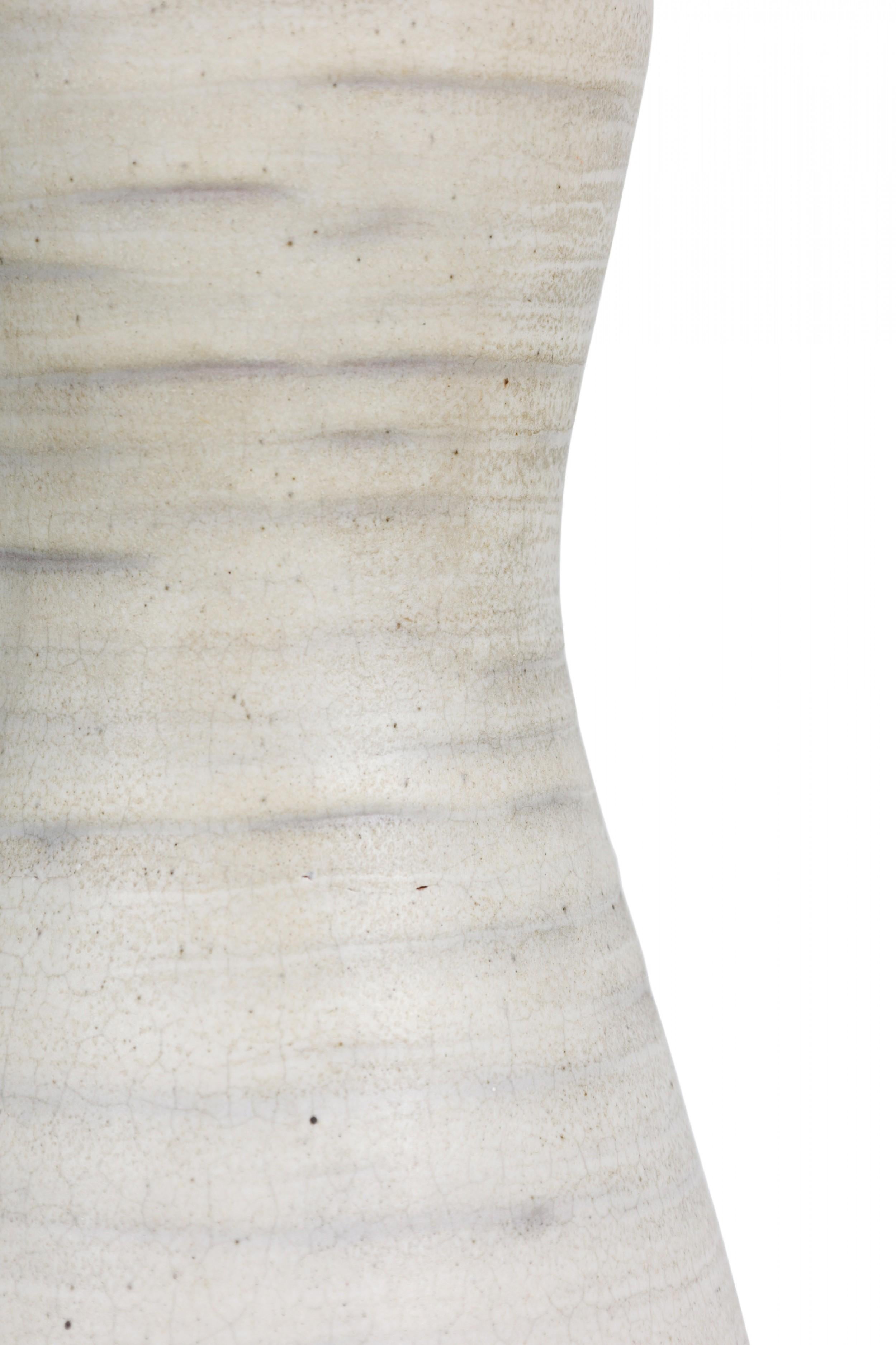Lampe de table en céramique américaine du milieu du siècle, de forme ovoïde, avec une tige en laiton encastrée et une prise d'interrupteur non fonctionnelle dépassant du sommet aplati, le corps subtilement nervuré, émaillé à la craie blanche avec