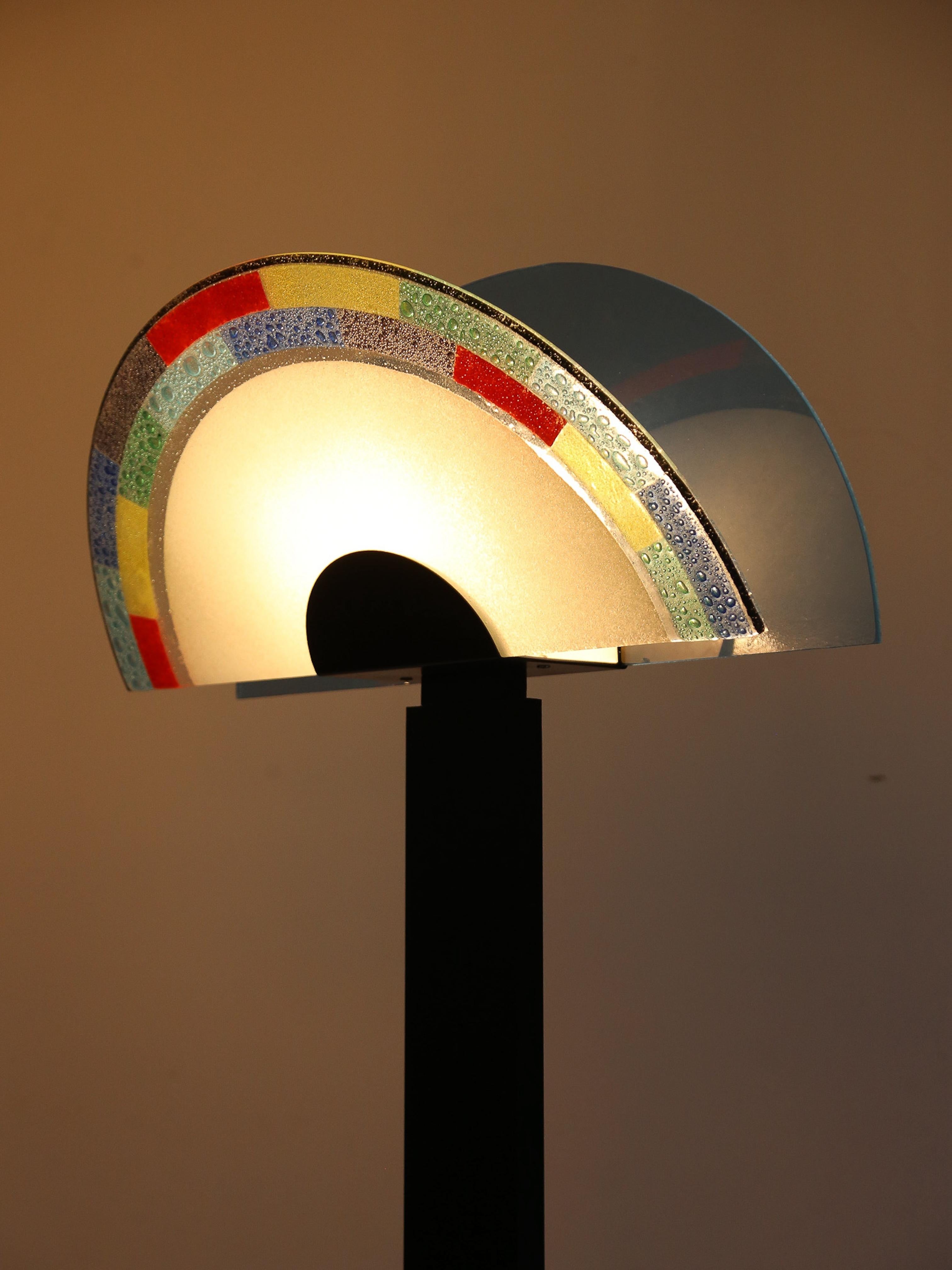 Fondée à Murano, la célèbre région verrière d'Italie, AV Mazzega associe l'artisanat traditionnel au design contemporain pour créer des pièces d'éclairage uniques.

L'abat-jour semi-circulaire en verre avec un motif coloré est caractéristique du