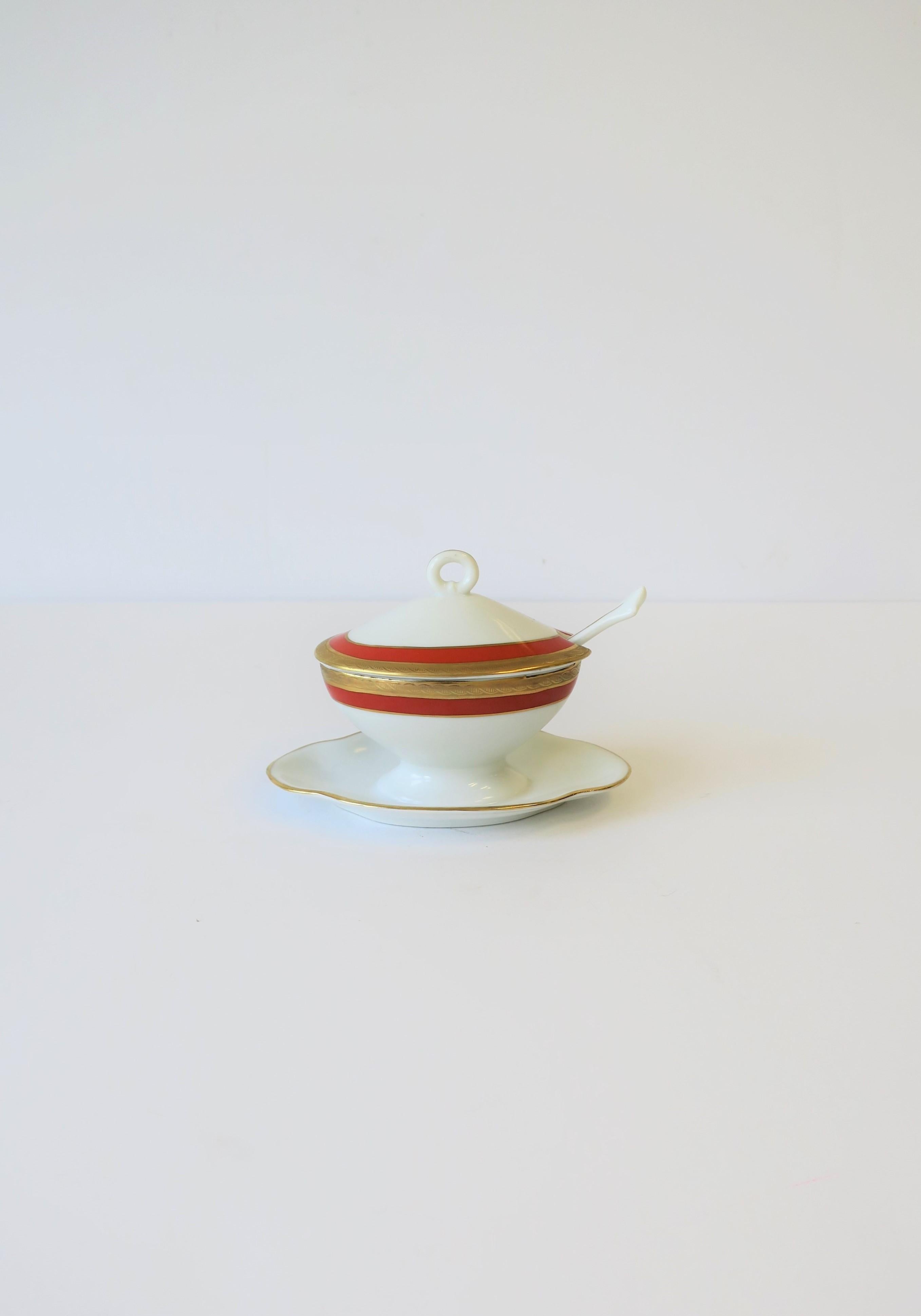 A beautiful Italian white and gold condiments dish/vessel with spoon by designer Richard Ginori, with decorative gold band and detail, circa mid-20th century, Italy. Colors include: white porcelain, gold gilt, and a red/orange accent band. With