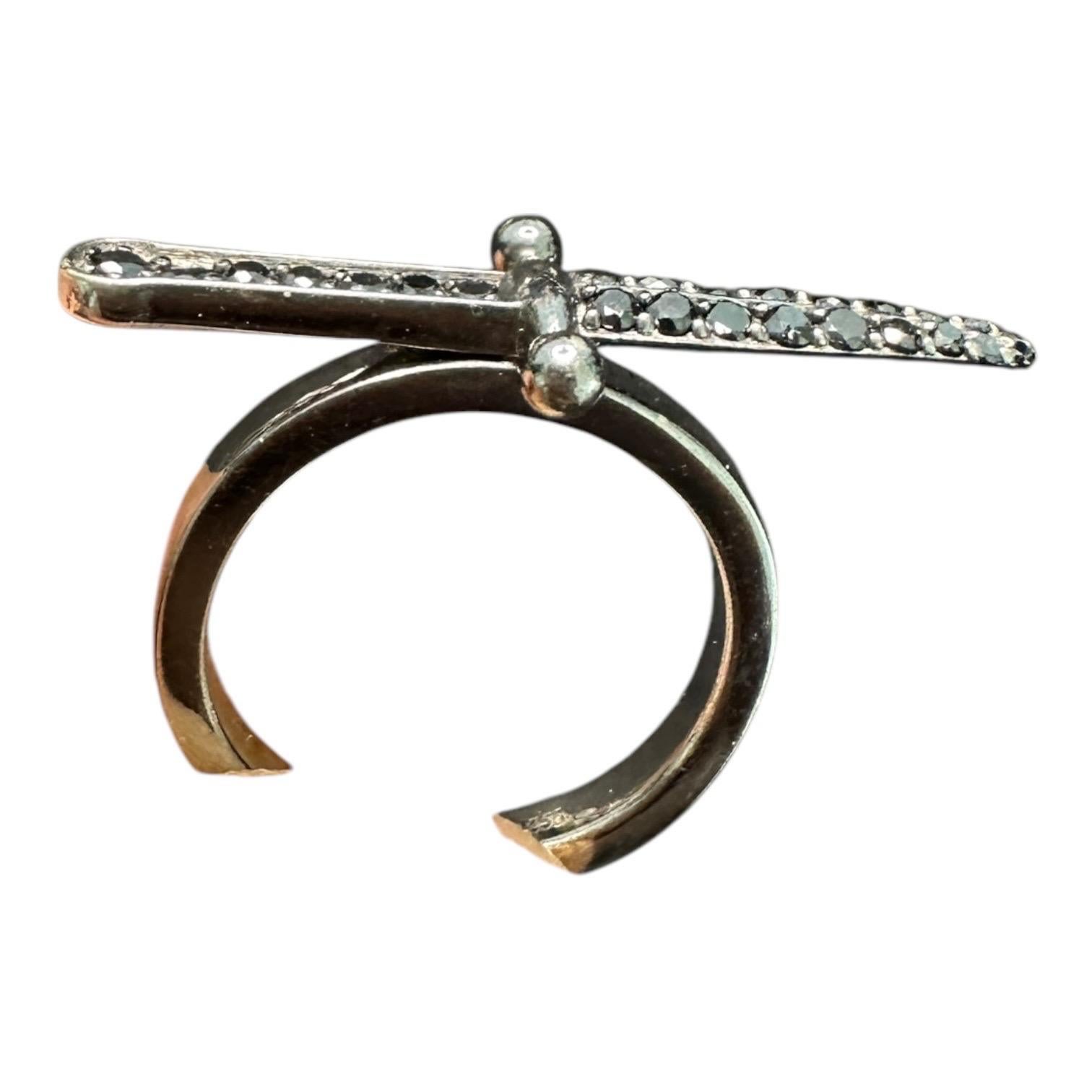 Anello a forma di pugnale in 18 carati realizzato dal designer di Hollywood JBH. L'anello è composto da diamanti neri in una montatura a baccello. L'anello misura 28,8 mm di lunghezza al pugnale e la larghezza è di 10,6 g. La misura è 5.5.


 