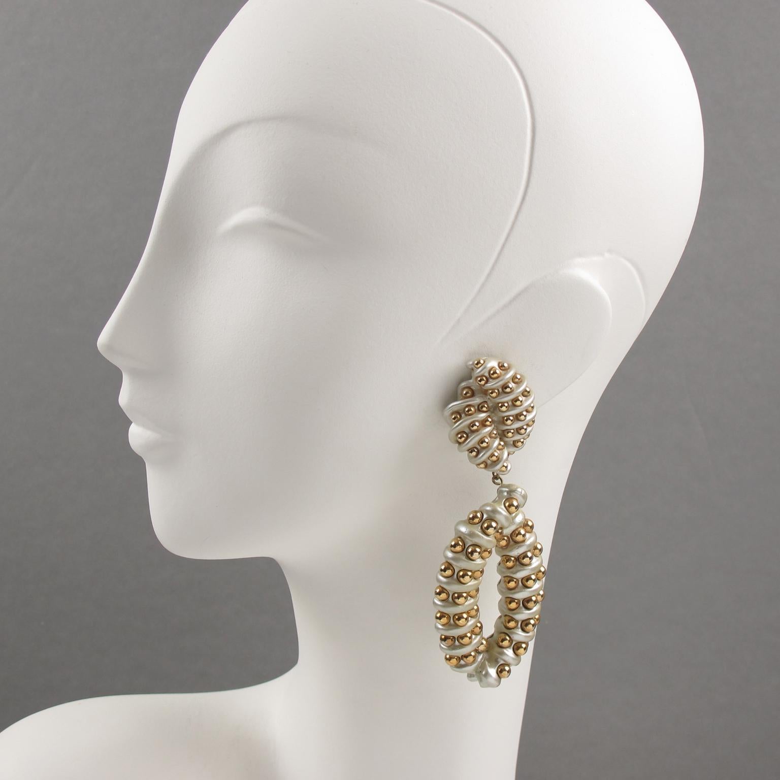 Impressive 1980s oversized chandelier clip-on earrings designed by Jewellians. They feature a spectacular shoulder-duster dangling shape with white pearlized resin ornate with gilded metal caviar seed beads. The Jewellians company logo is at the