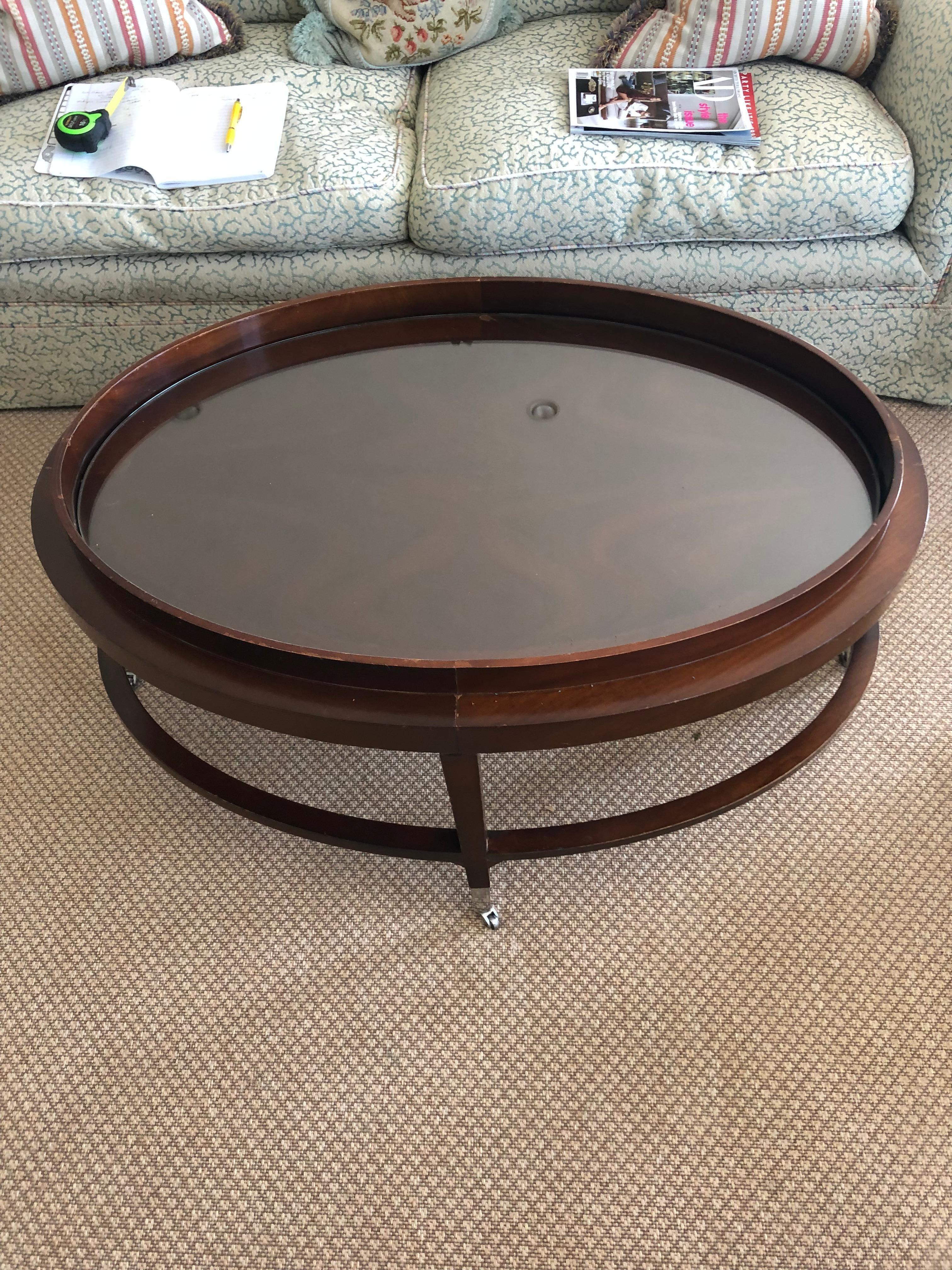 Une table basse ovale de grande taille avec un insert en verre dans une table en acajou terminée par des roulettes en nickel.