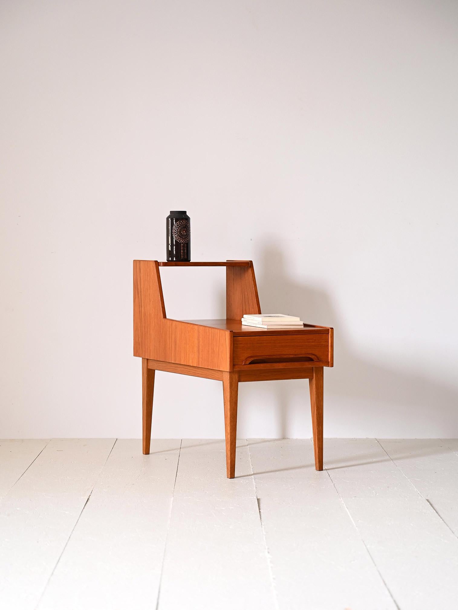 Scandinavian teak nightstand with drawer.

Particular piece of Swedish modernism from the 1960s consisting of a double shelf. There is a convenient drawer with a carved wooden handle.
Tapered legs slender the figure and recall the square, bold