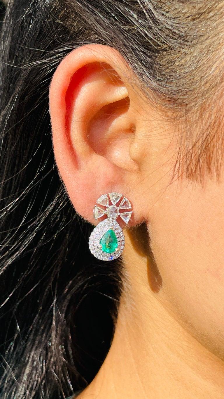These exquisite earrings are crafted in 14k white gold, showcasing a luxurious combination of vibrant emeralds and sparkling diamonds. Each earring features a striking pear-shaped emerald, weighing a total of 1.41 carats, beautifully framed by a