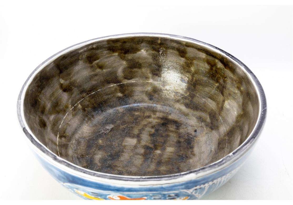 Signed Desimone on the base and the side. An amusing folk style decorated large center bowl with colored fish and fishermen on blue ground. Mottled gray glazed inside. Retailed by Gumps. 
Diam. 14 1/4