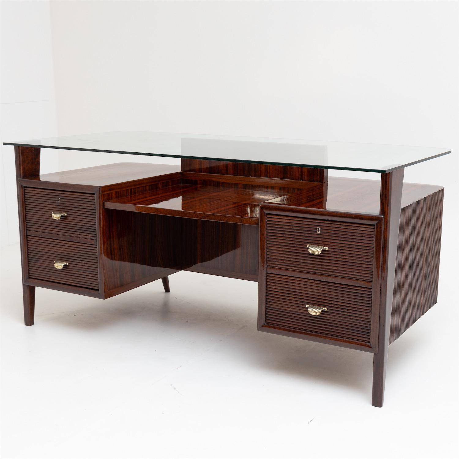 Large desk with D-shaped glass top and four drawers with brass handles. The surface of the back and the drawer fronts have vertical and horizontal ribbing respectively. The desk can be placed freely in the room and has been professionally restored.