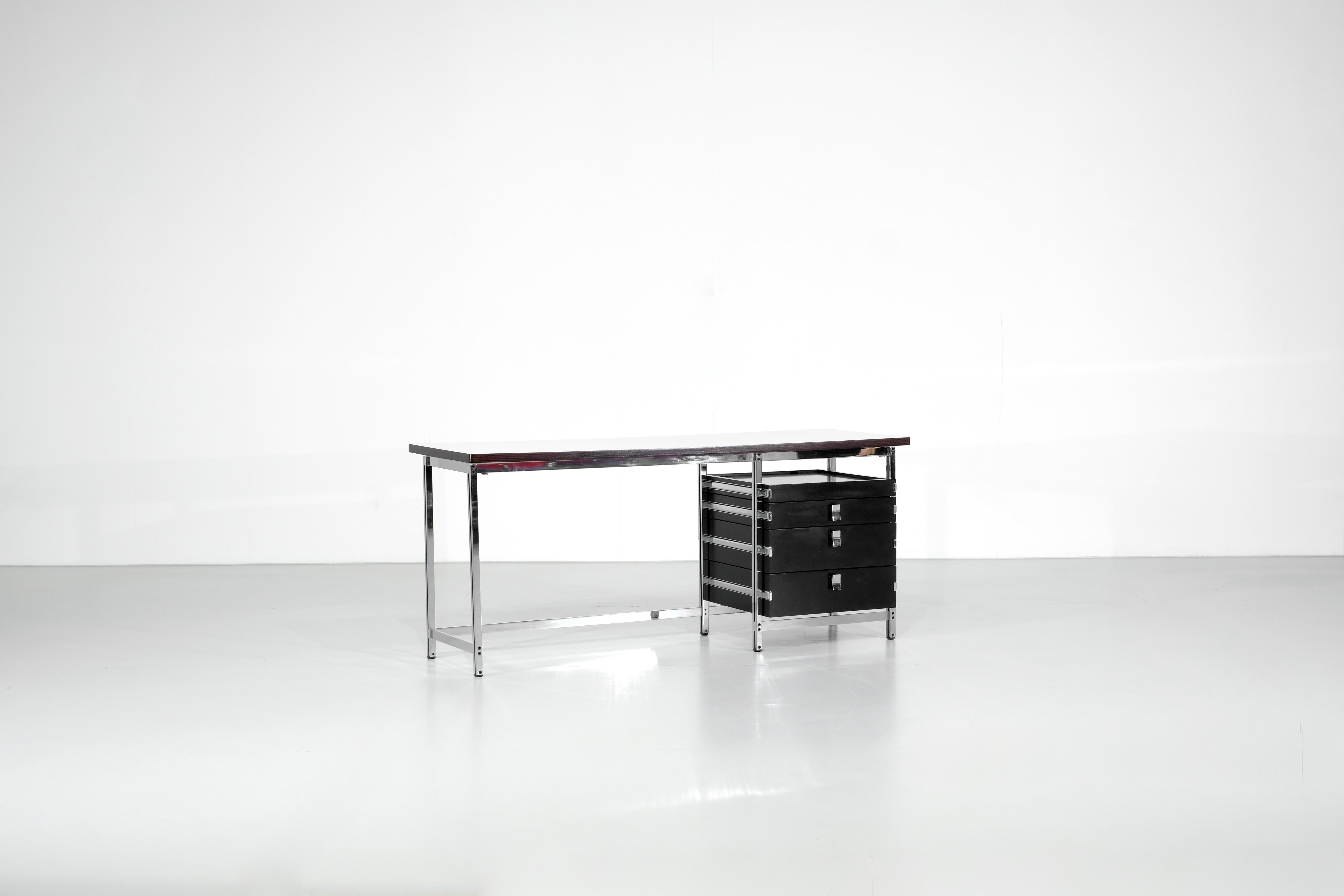 Scrivania in legno con piano in laminato bianco su struttura in acciaio cromato. 
Un nero  piedistallo con tre cassetti e un cassetto, maniglie firmate 
