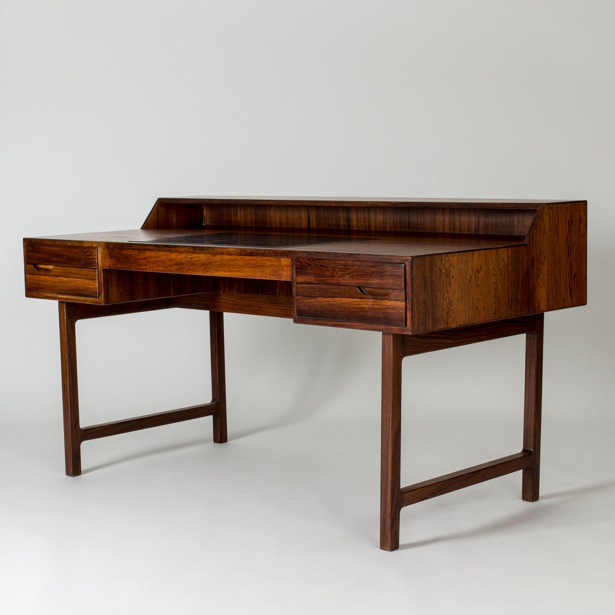 Very cool desk by Kurt Østervig, made from rosewood with a built-in shelf. Bold lines and beautiful woodgrain. Inlayed black leather writing pad.

Size: Height 72.5 / 82 cm, Width 149.5 cm, Depth 74.5 cm.