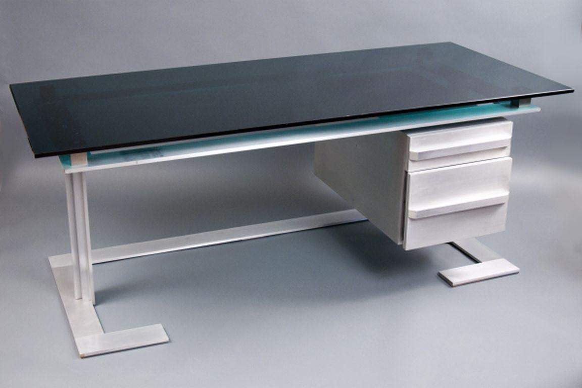 Brushed steel frame enclosing two mahogany drawers, faced with aluminum and inset with a dark-green tinted glass work surface. The top drawer locks.

